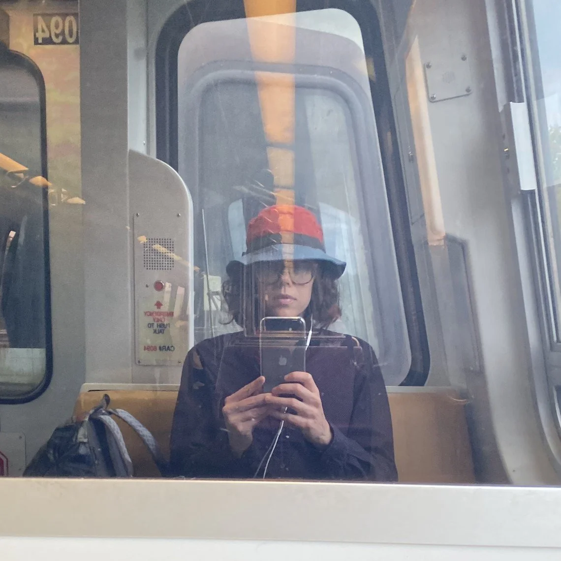 Kate Gorman taking a selfie of her reflection in a window while riding the subway