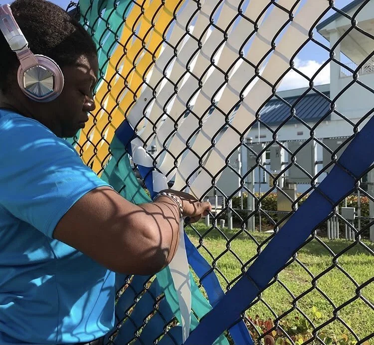 The Black Dalhia weaving colorful stripes of plastic into a fence