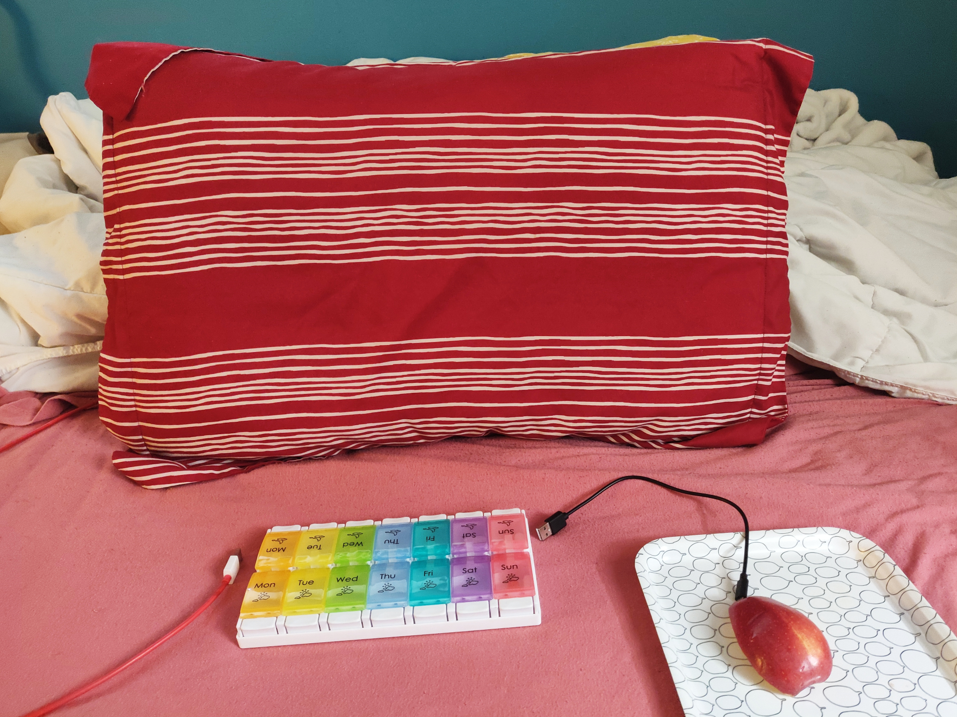 A photograph of a “computer” made out of other objects. The screen is a pillow, the keyboard a pill minder, the mouse is part of an apple on a rectangle plate that serves as a mousepad.