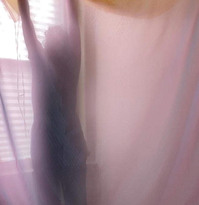 The silhouette of a woman with her arm raised above her head, behind a hanging piece of  lilac organza