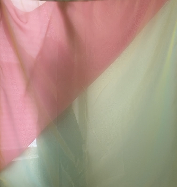 The faint silhouette of a woman behind layered pieces of pink, blue, and yellow organza