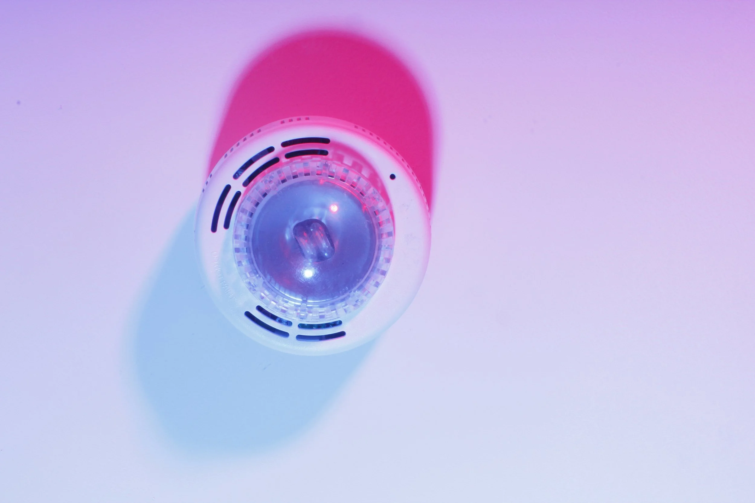 A photo of a flashing fire alarm. The lightning and angle of the photo give the image an abstracted look.