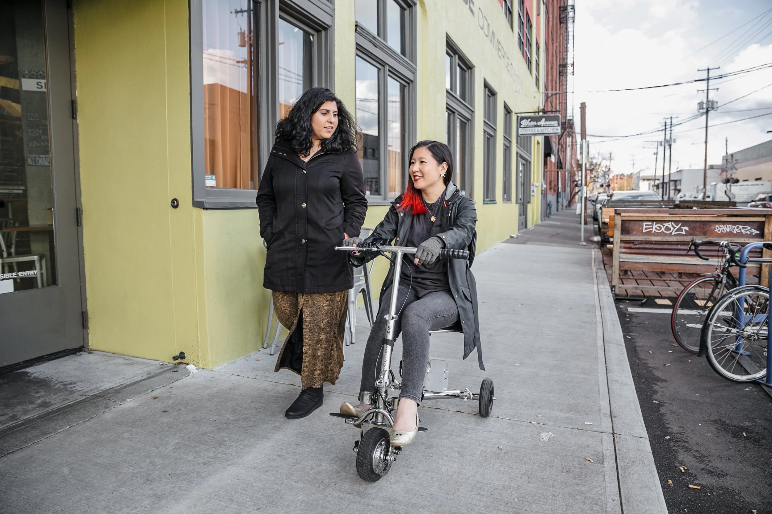 Two friends chatting while on the sideway - one walking and the other using an electric mobility scooter
