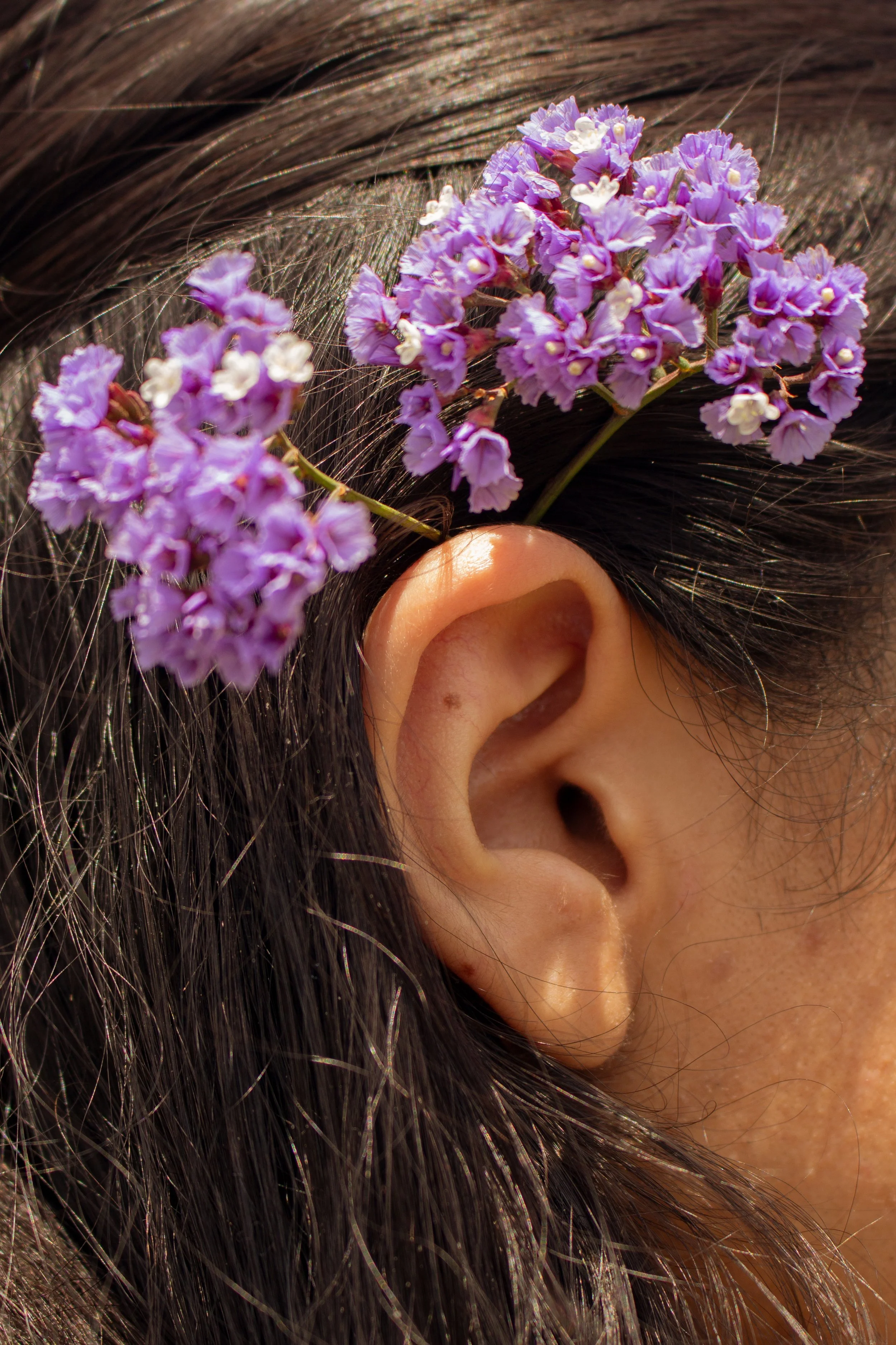 An ear, covered partially by long hair, with a couple of little flowers sitting up on top.