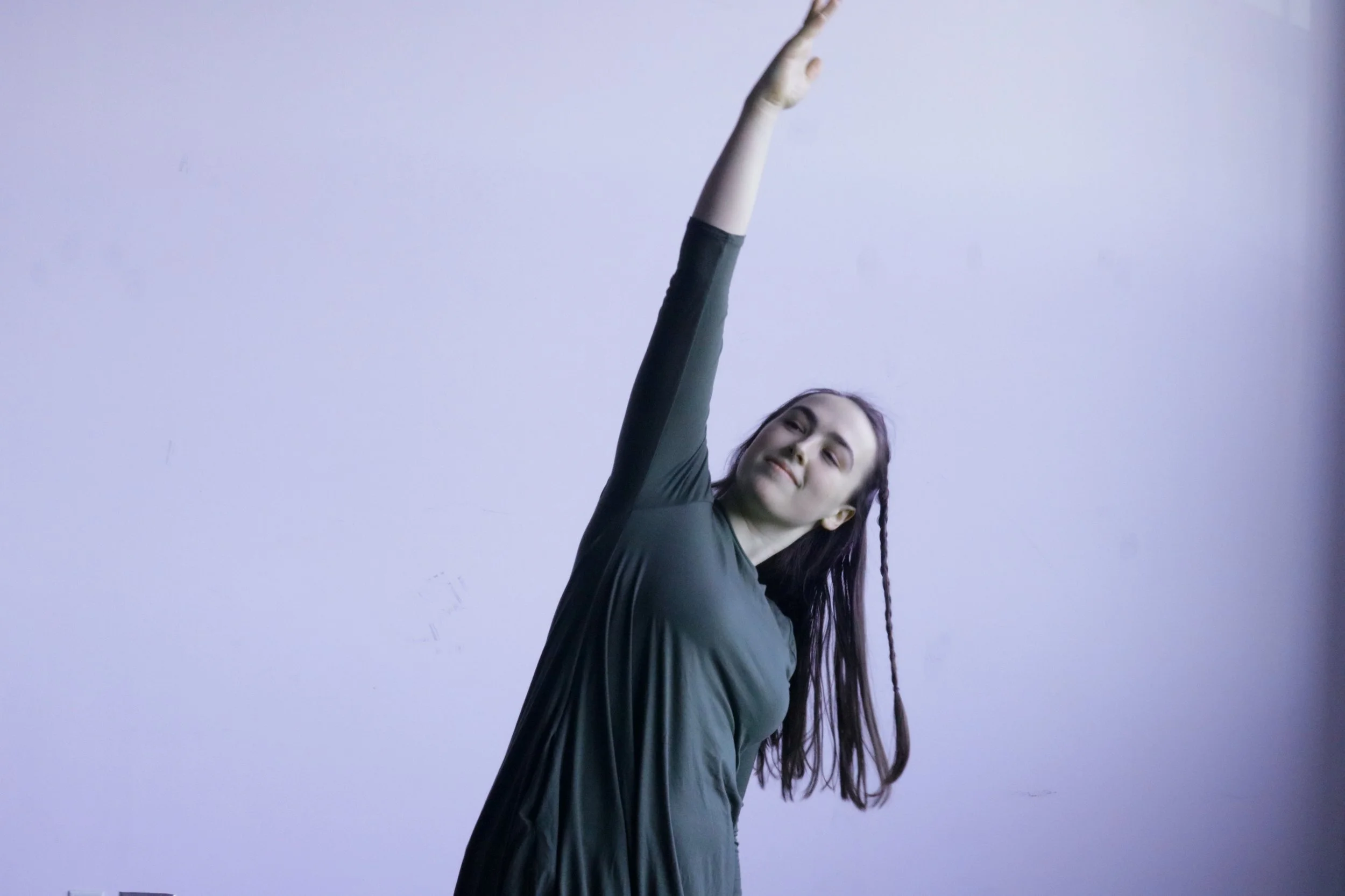 A white woman with long brown hair leans over to the side with one arm arching over her head.