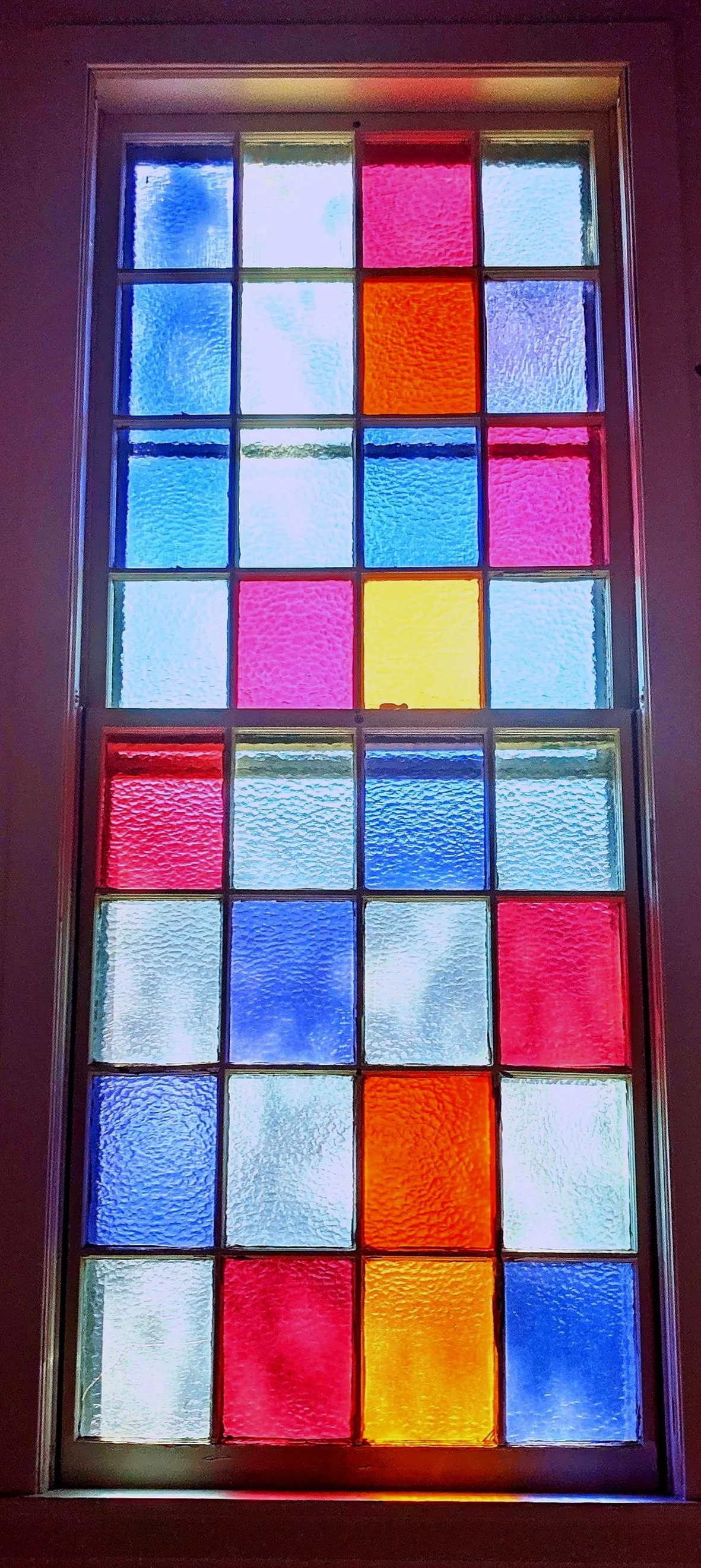 A tall grid glass window with brightly colored glass panels