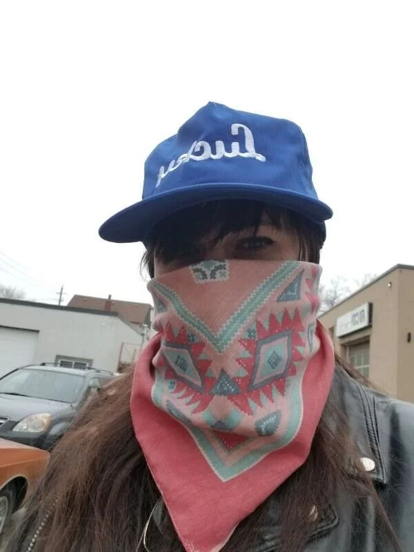 Tessa Shank wearing a blue baseball hat and patterned bandana, covering her mouth and nose.