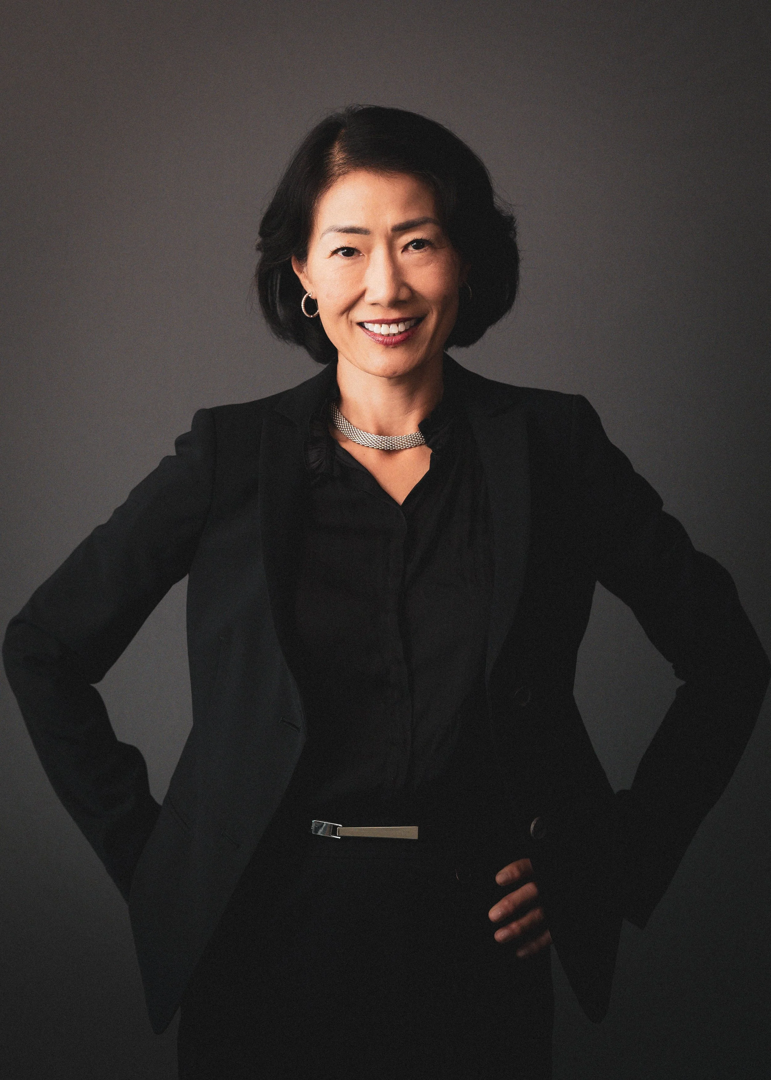 Headshot of a smiling woman with shoulder-length dark hair, wearing a pearl necklace and a black top.
