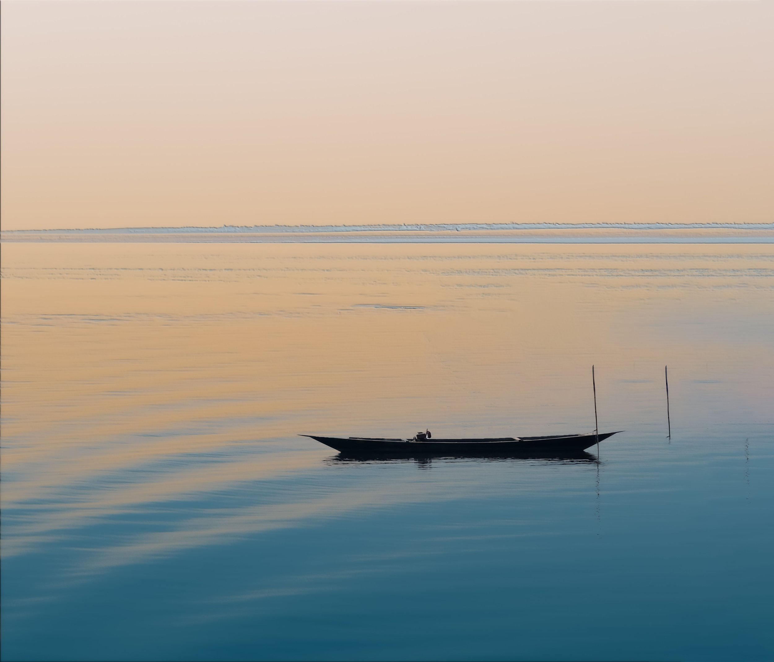 A boat floating on calm water during sunset or sunrise with a soft, pastel-colored sky in the background.
