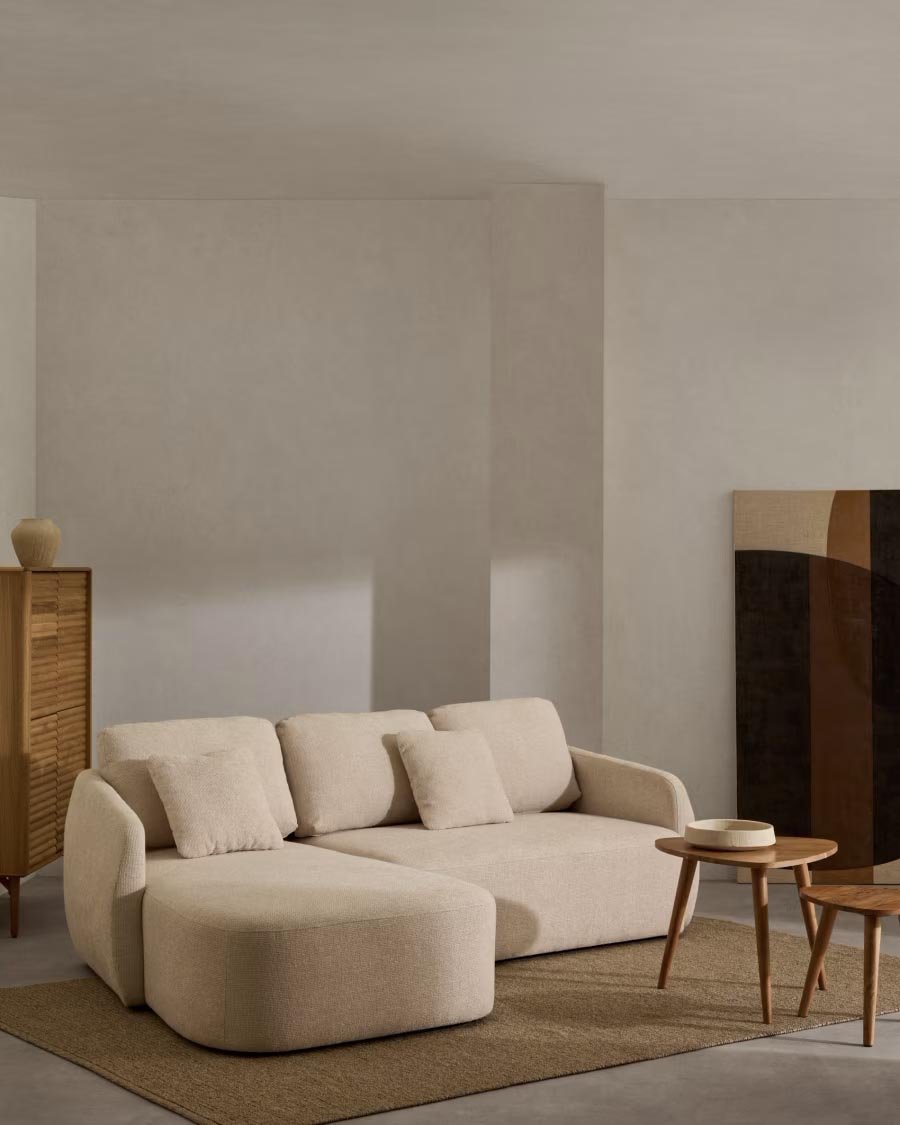 Salotto con divano beige, tavolino e credenza in legno, pareti chiare e pavimento in cemento, decorazioni minimaliste.