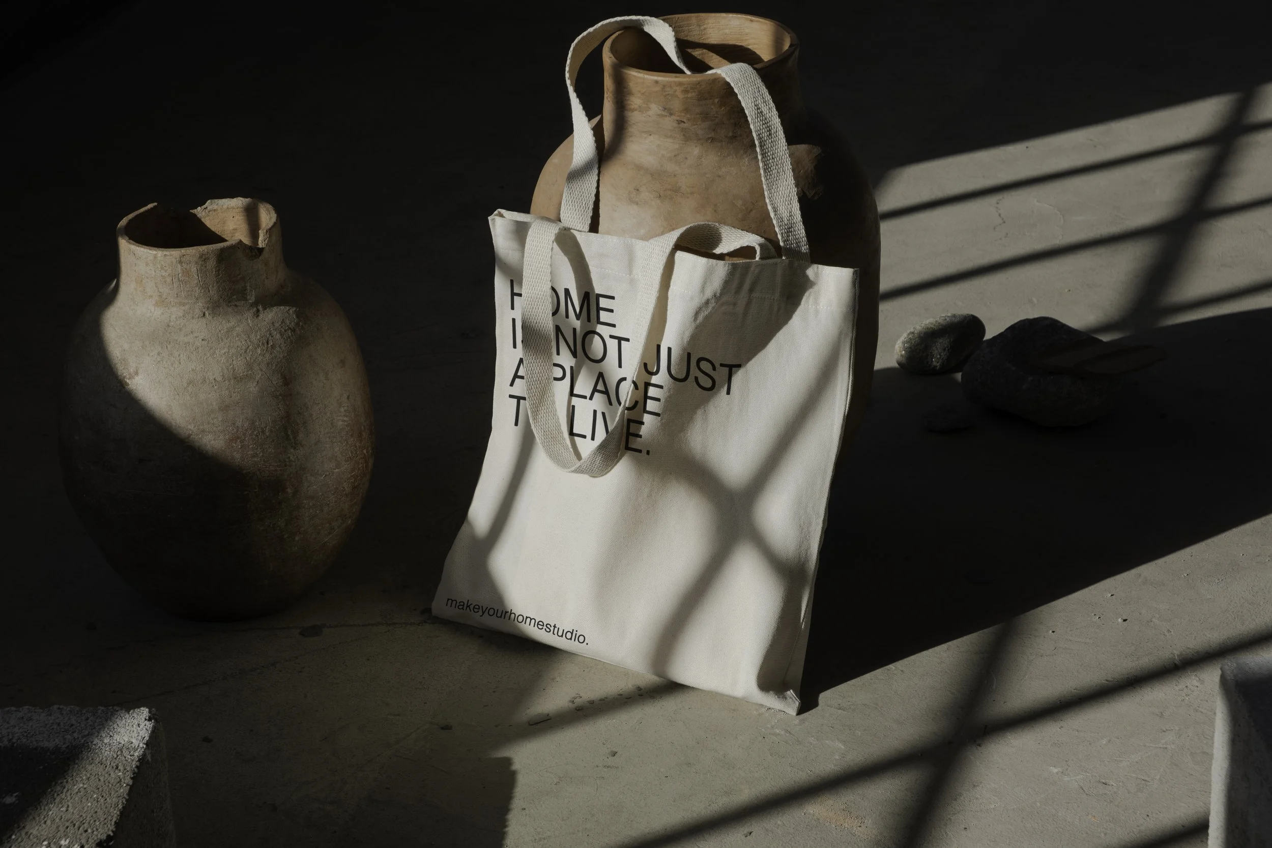 Vasi di terracotta e una borsa di stoffa con scritte, con ombre e luce naturale che creano linee di ombra sul pavimento.