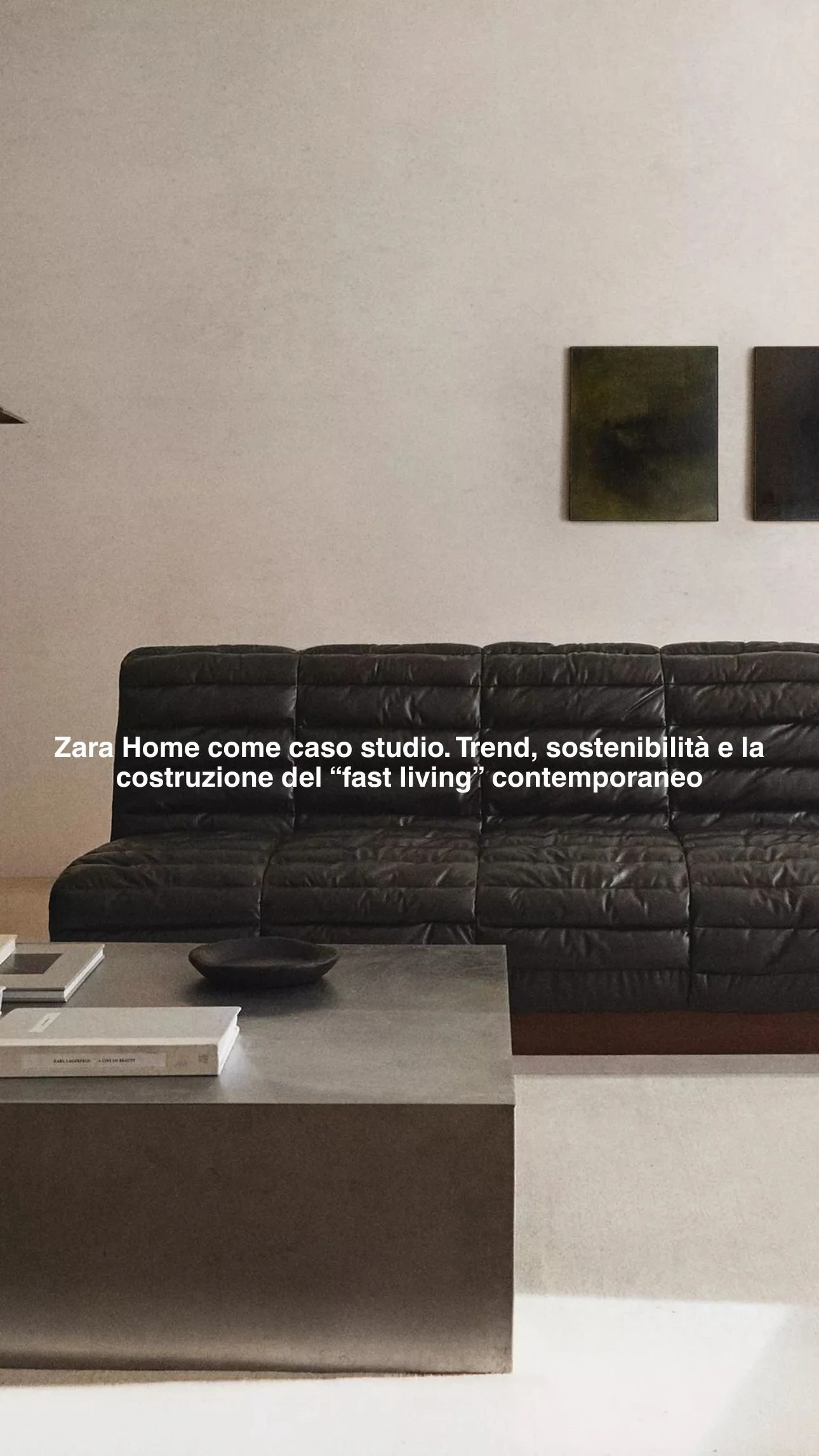 Interno di un soggiorno con un divano nero in pelle, un tavolino in pietra con alcuni libri e una ciotola nera, pareti beige, decorazioni minimal e due quadri sovrapposti.