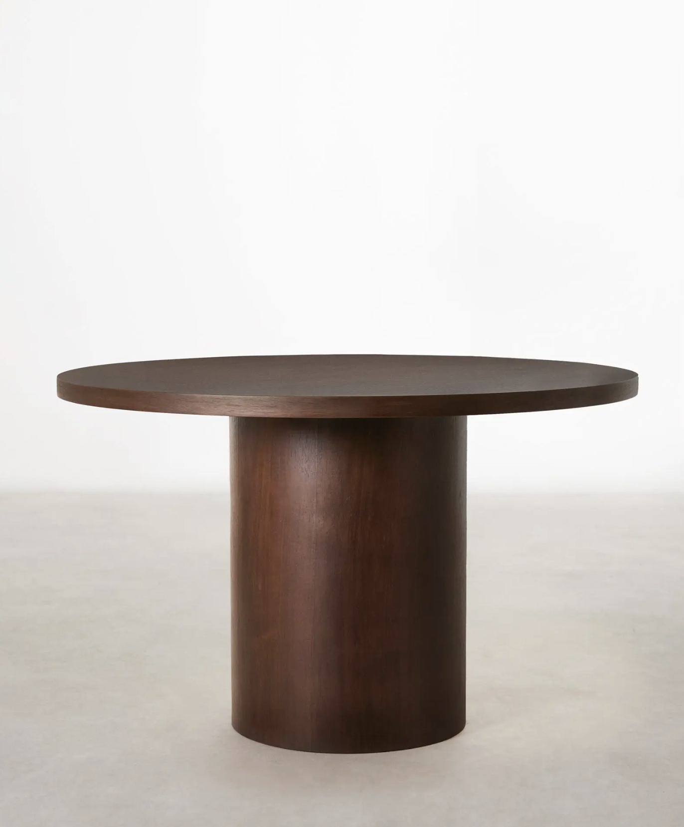 Tavolo rotondo in legno scuro con base cilindrica, posizionato su una superficie chiara, sfondo bianco