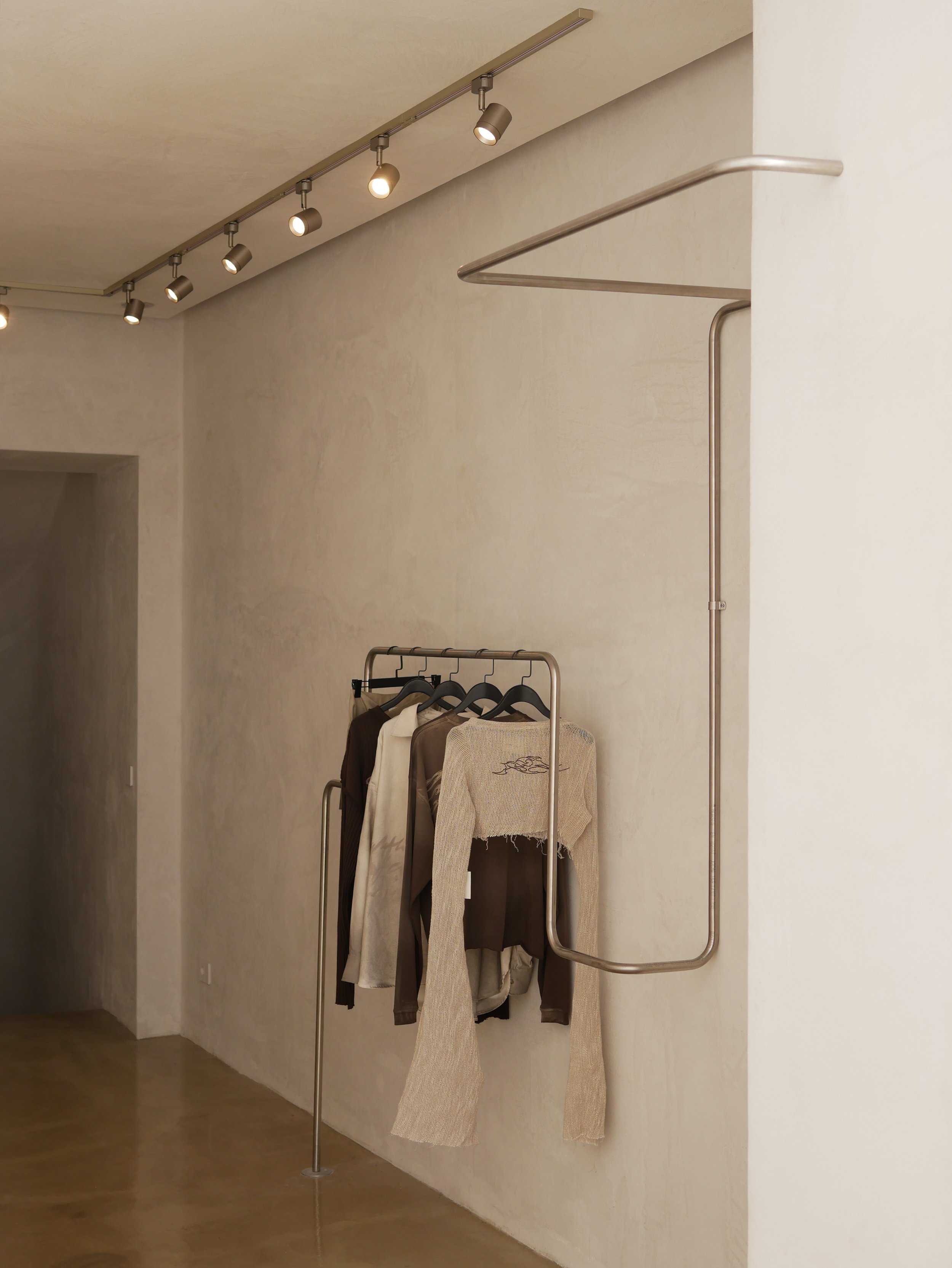 Ripiano di abbigliamento con alcuni vestiti appesi a sostegno in una stanza con pareti beige e pavimento in legno.