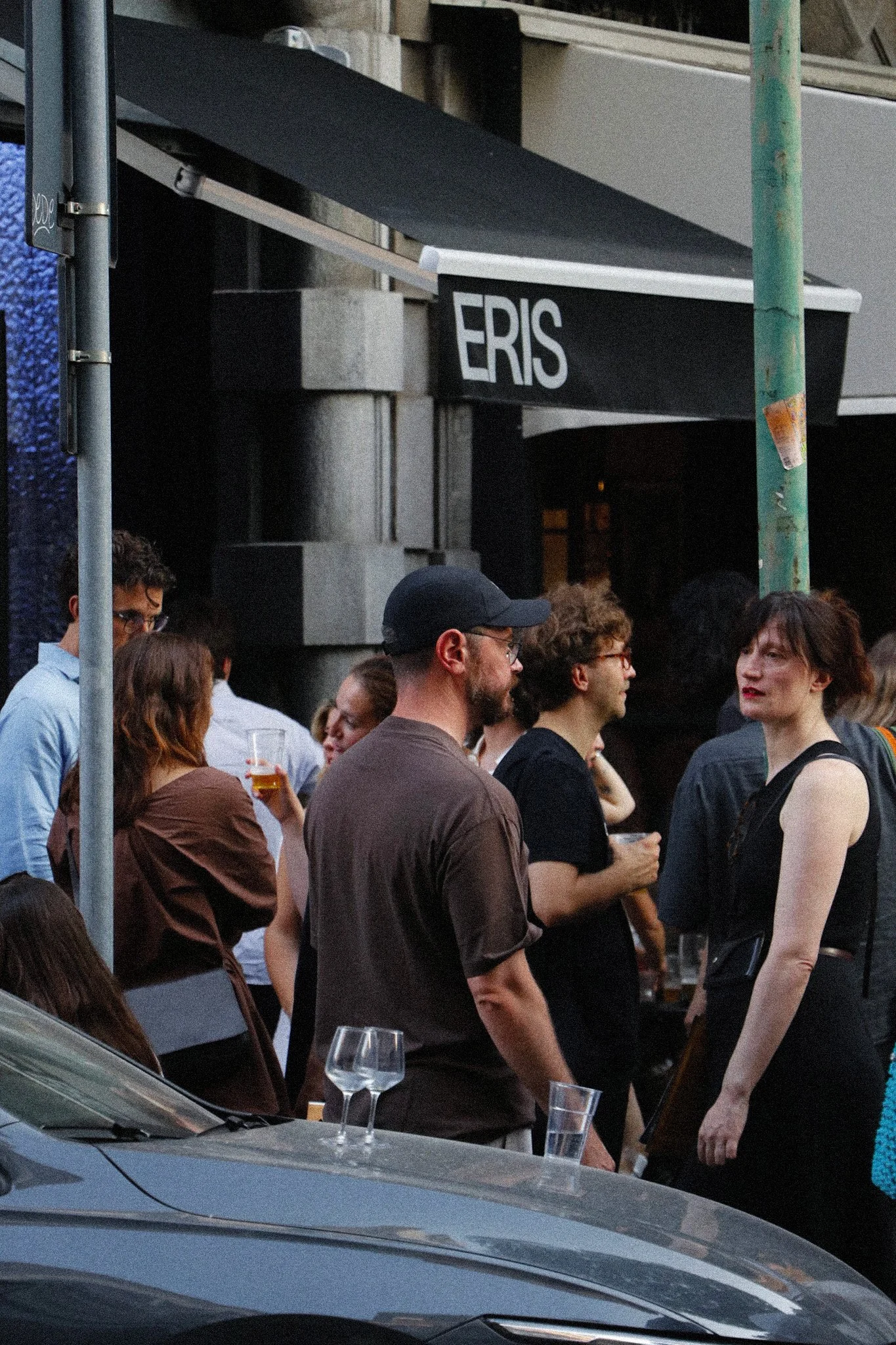 Un gruppo di persone che si incontrano e parlano all'aperto, con alcune persone che tengono bicchieri di bevande, in un ambiente urbano di sera.