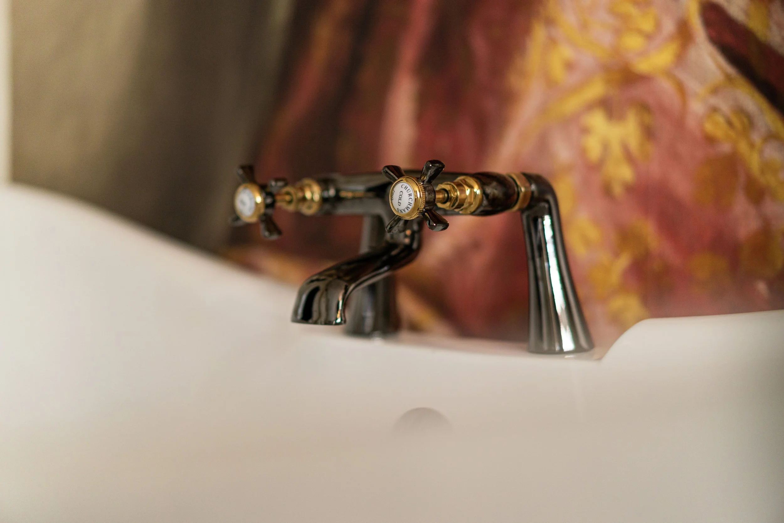Vintage bathroom faucet with gold and black detailing, set against a blurred ornate background.