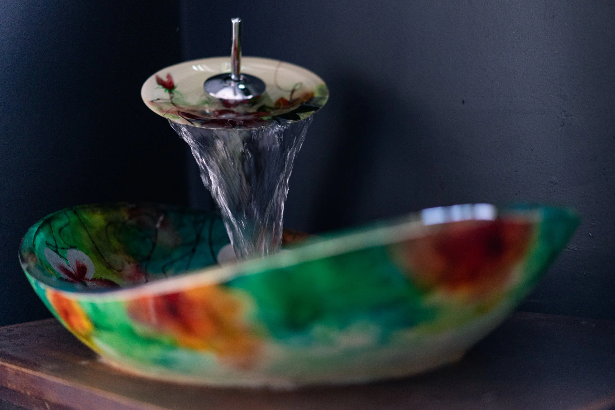 Colorful bowl-shaped sink with water flowing from a decorative faucet against a dark background.