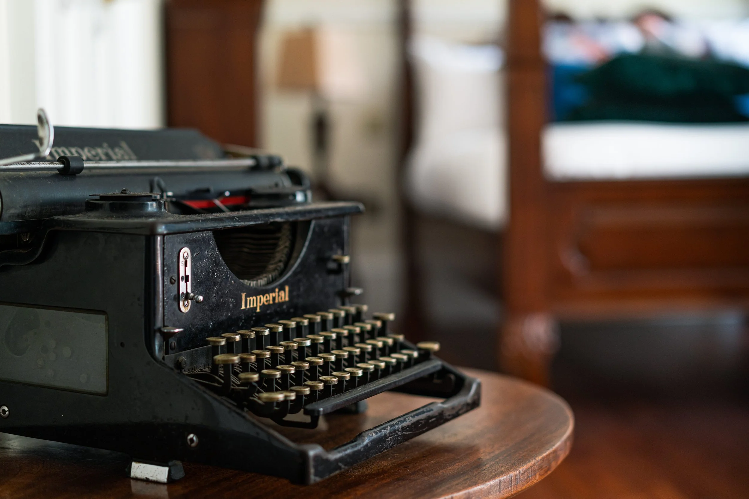 Antique black Imperial typewriter on a wooden table in a vintage room setting.