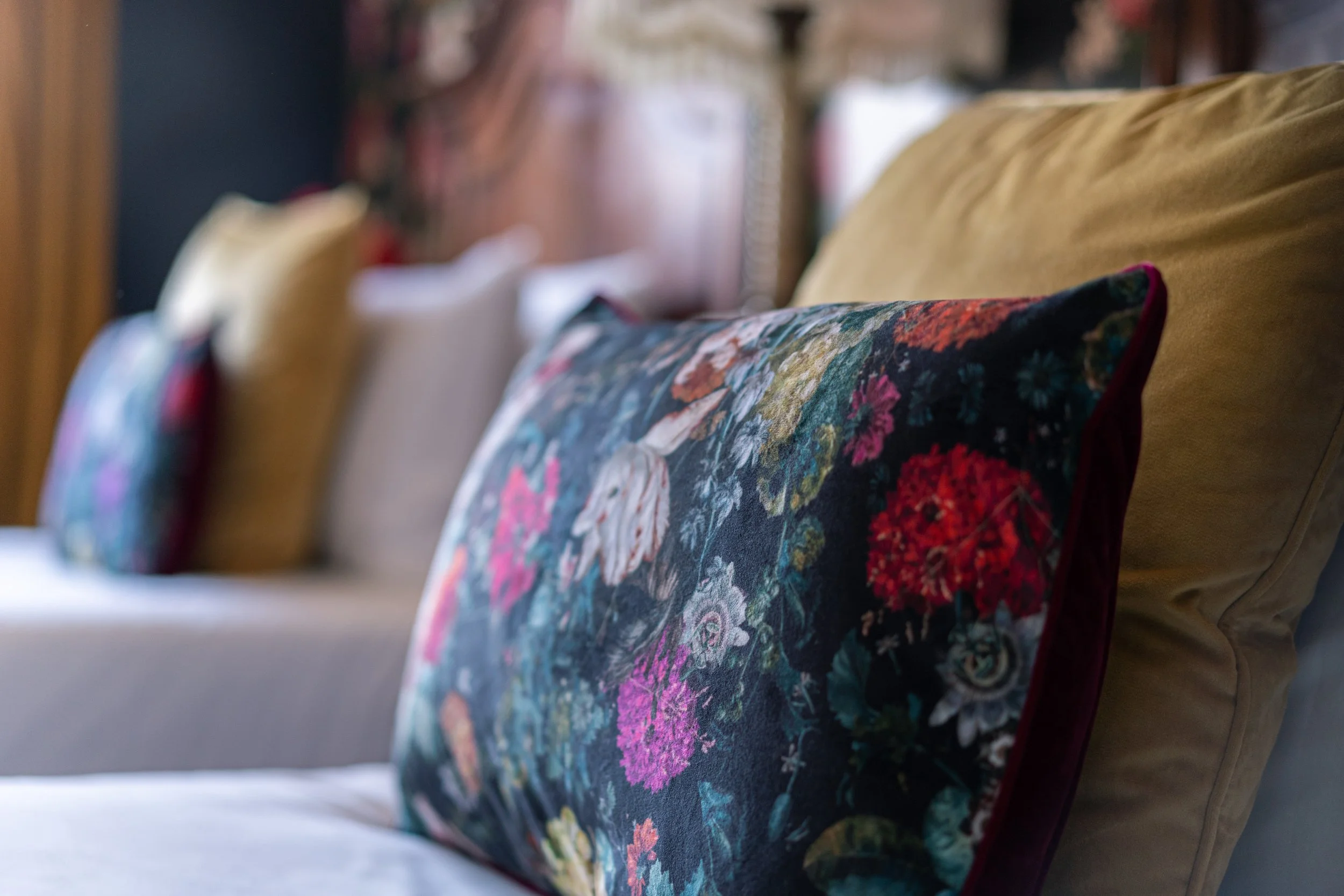 Close-up of a floral-patterned pillow on a sofa with various solid-colored pillows in the background.