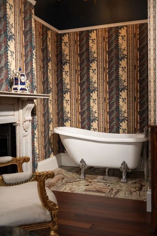 Vintage bathroom with clawfoot bathtub, ornate wallpaper, marble flooring, and a decorative fireplace mantel.