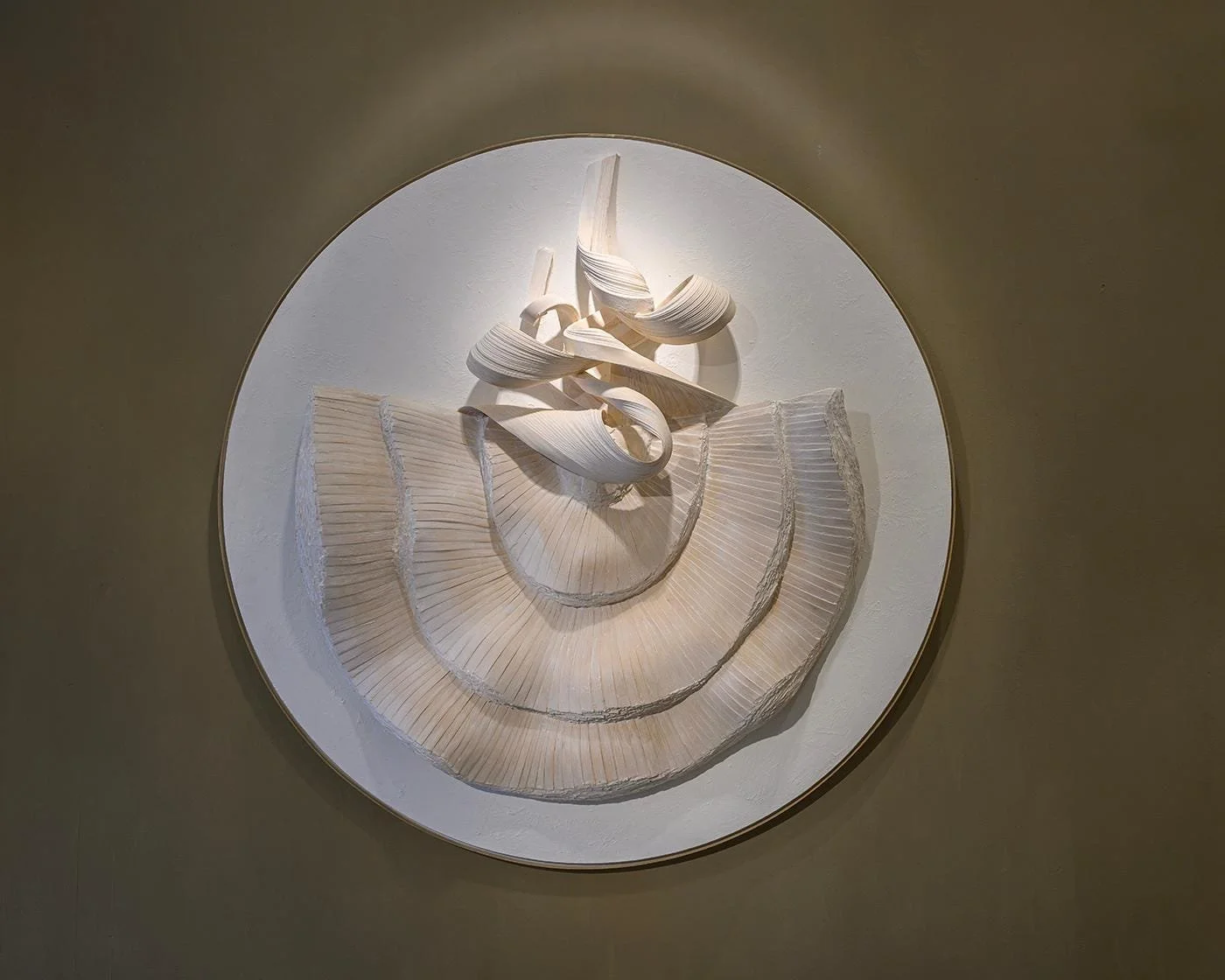 Round white relief with flowing ribbon forms above a pleated arc, by Michel Mullèr