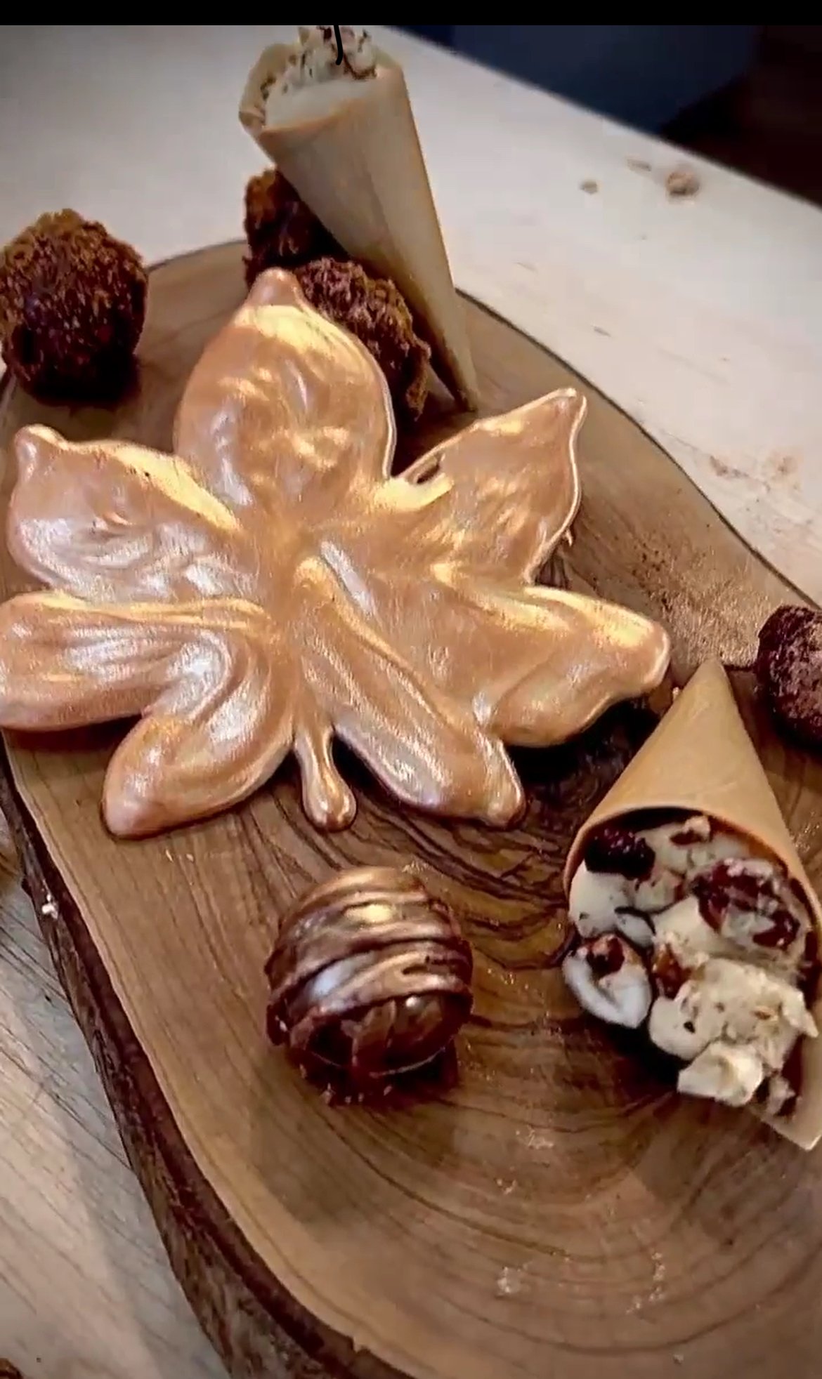 hand crafted chocolate leaf with a shimmering bronze finished next to a mini cone filled with spiced caramel , beautifully presented on a