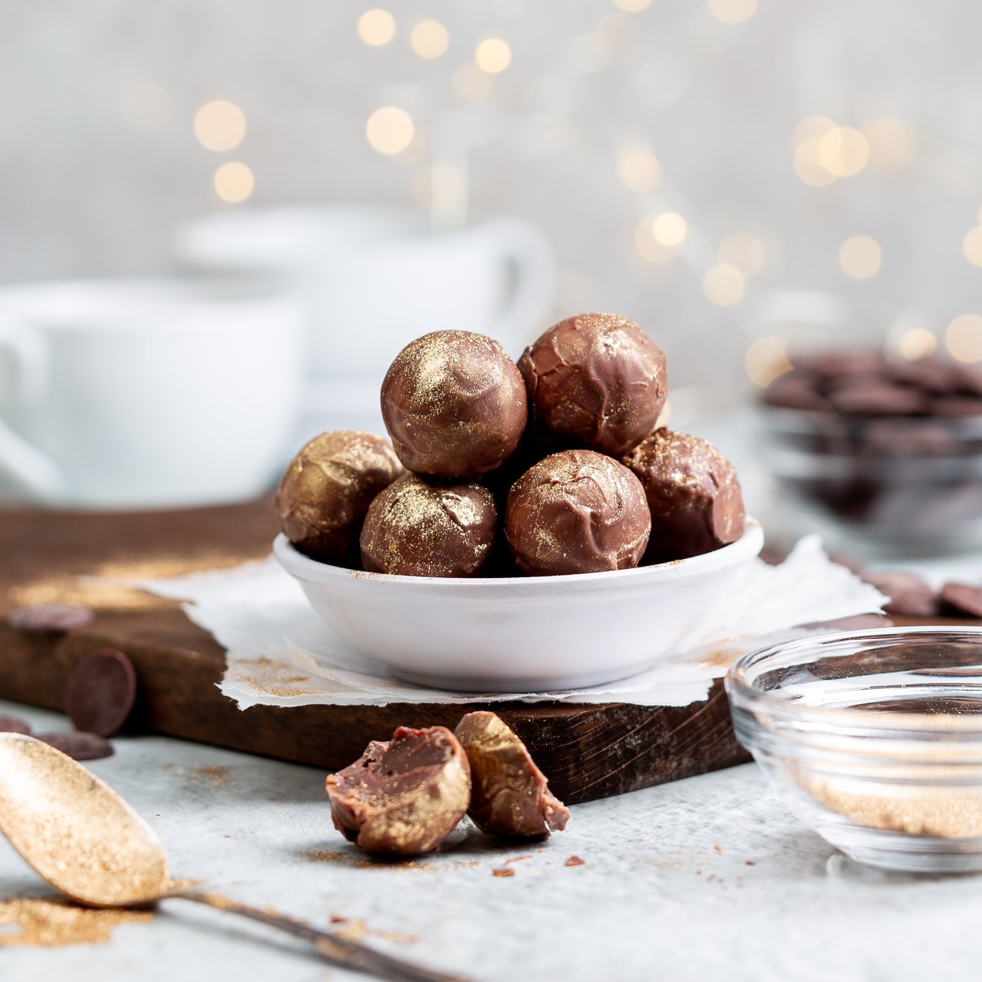 Handmade chocolate truffles dusted with edible gold displayed in a whiter bowl