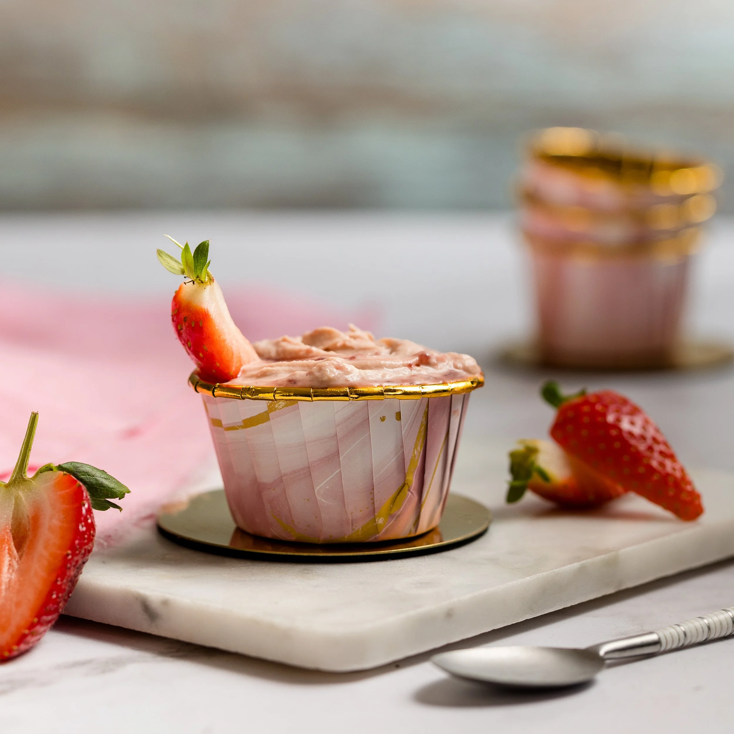 strawberry whitre chocolate cheese cake in a pink and gold pot sat on marble with a spoon and pieces of strawberries around the out side