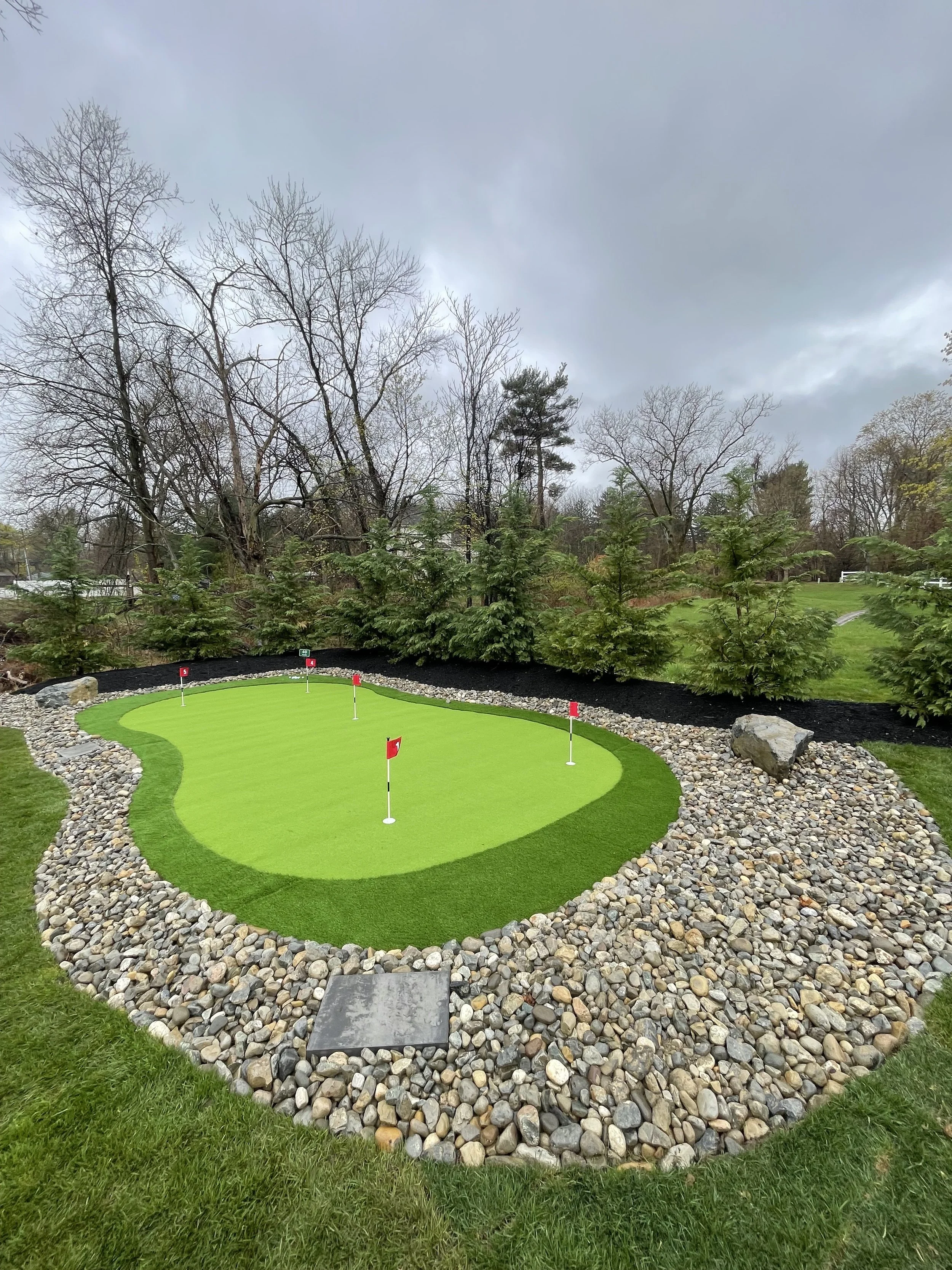 Miniature golf course with a putting green surrounded by rocks and trees with overcast sky.