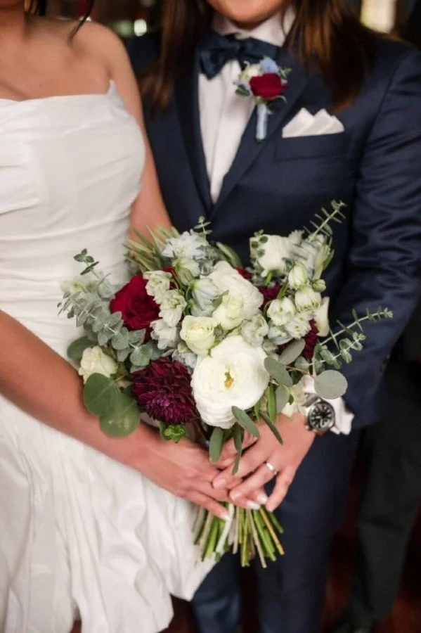 Queer couple holds bouquet of red and white flowers during their intimate Korean wedding.