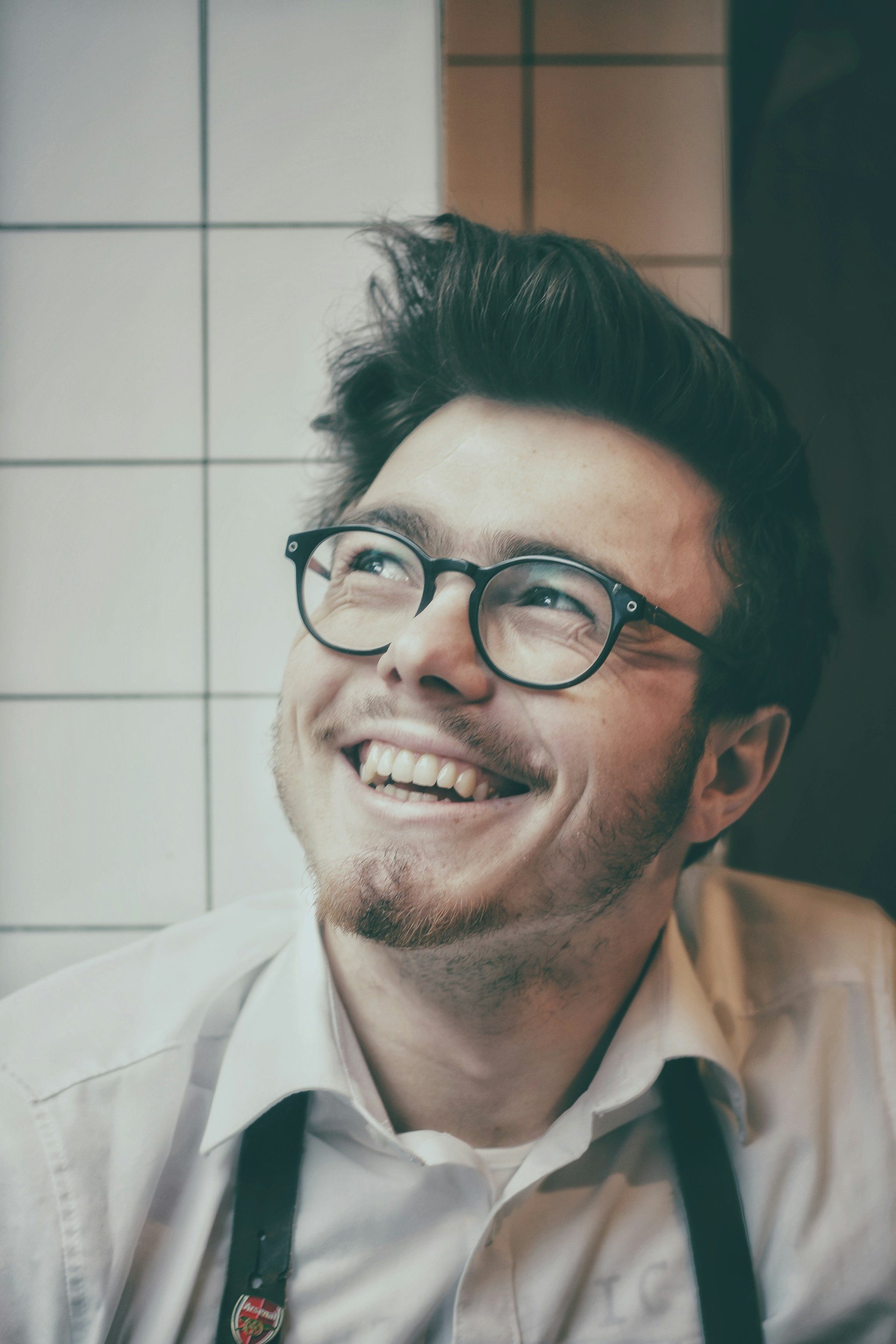 young man with glasses and dark hair. Smiling and looking up.