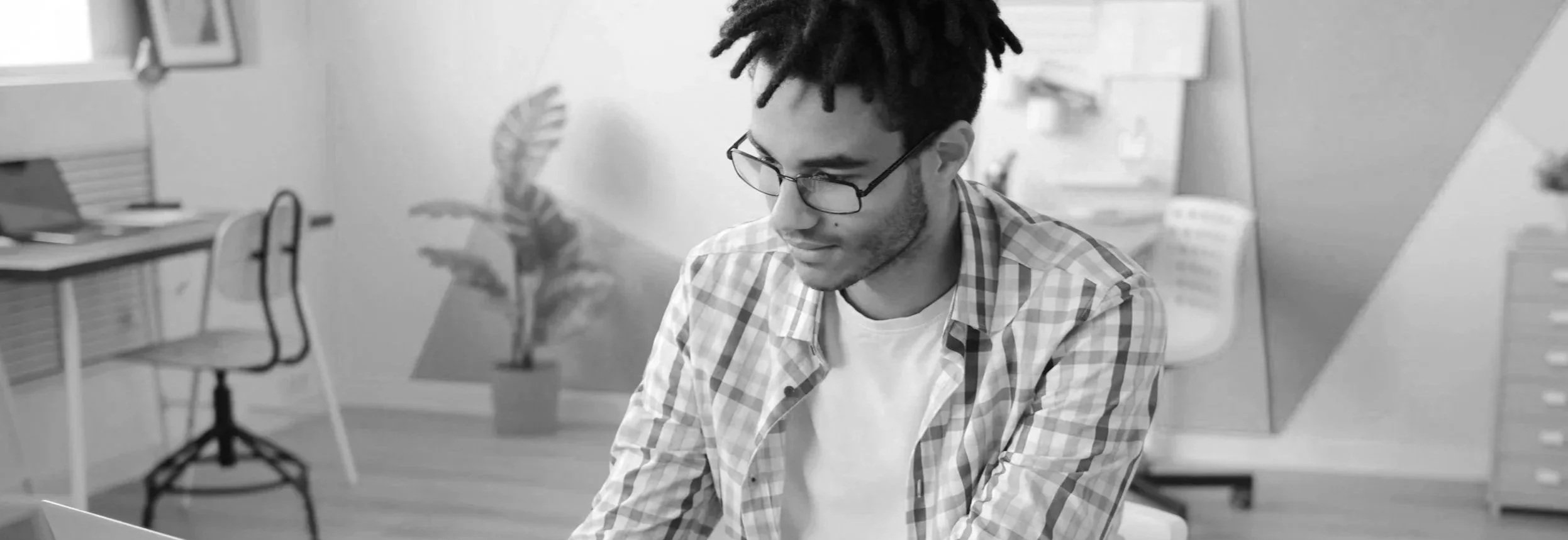 a black man with glasses and  locs working on his computer.