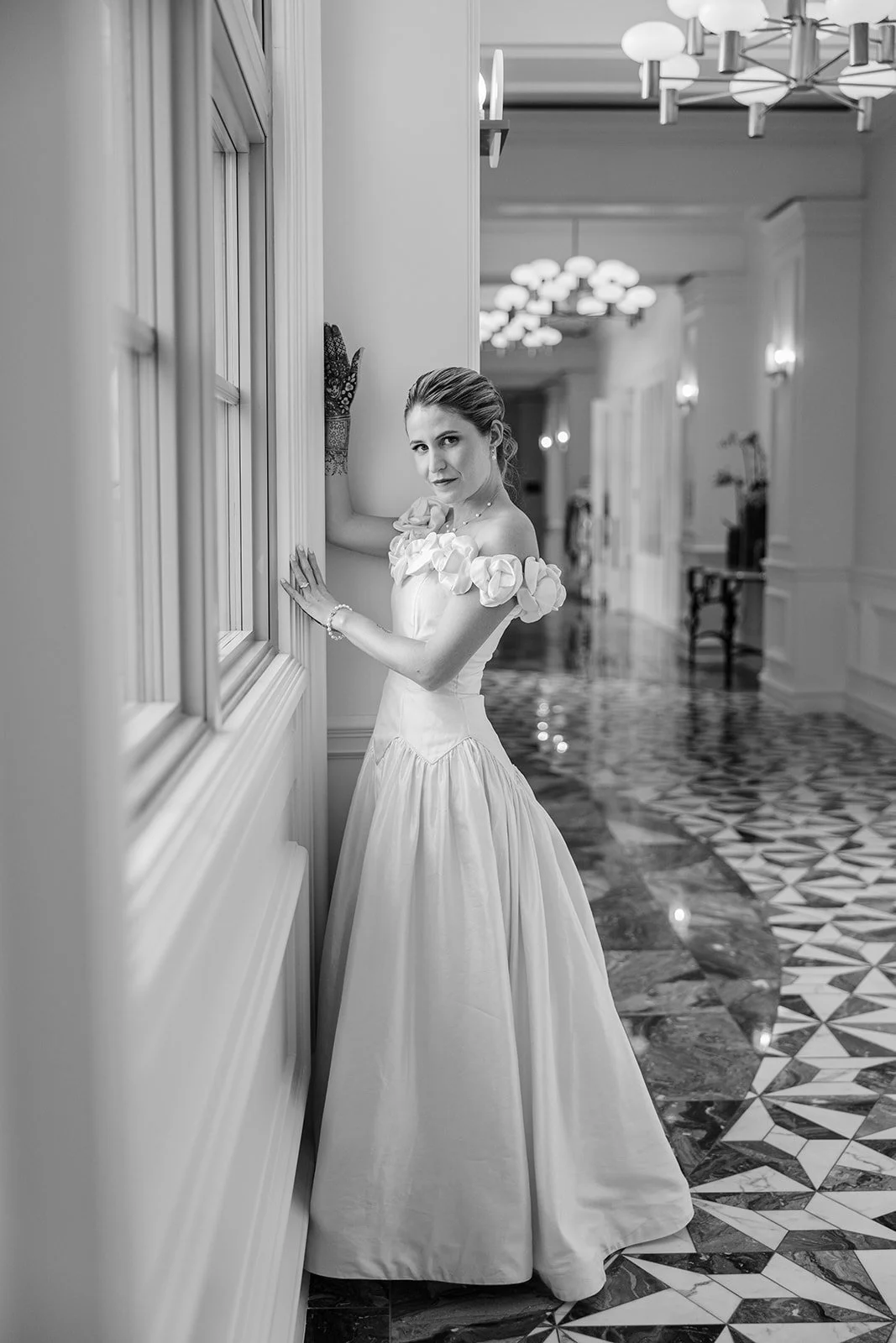 A bride strikes a dramatic pose in her off-the-shoulder ballgown, posing in a Deco-inspired interior.