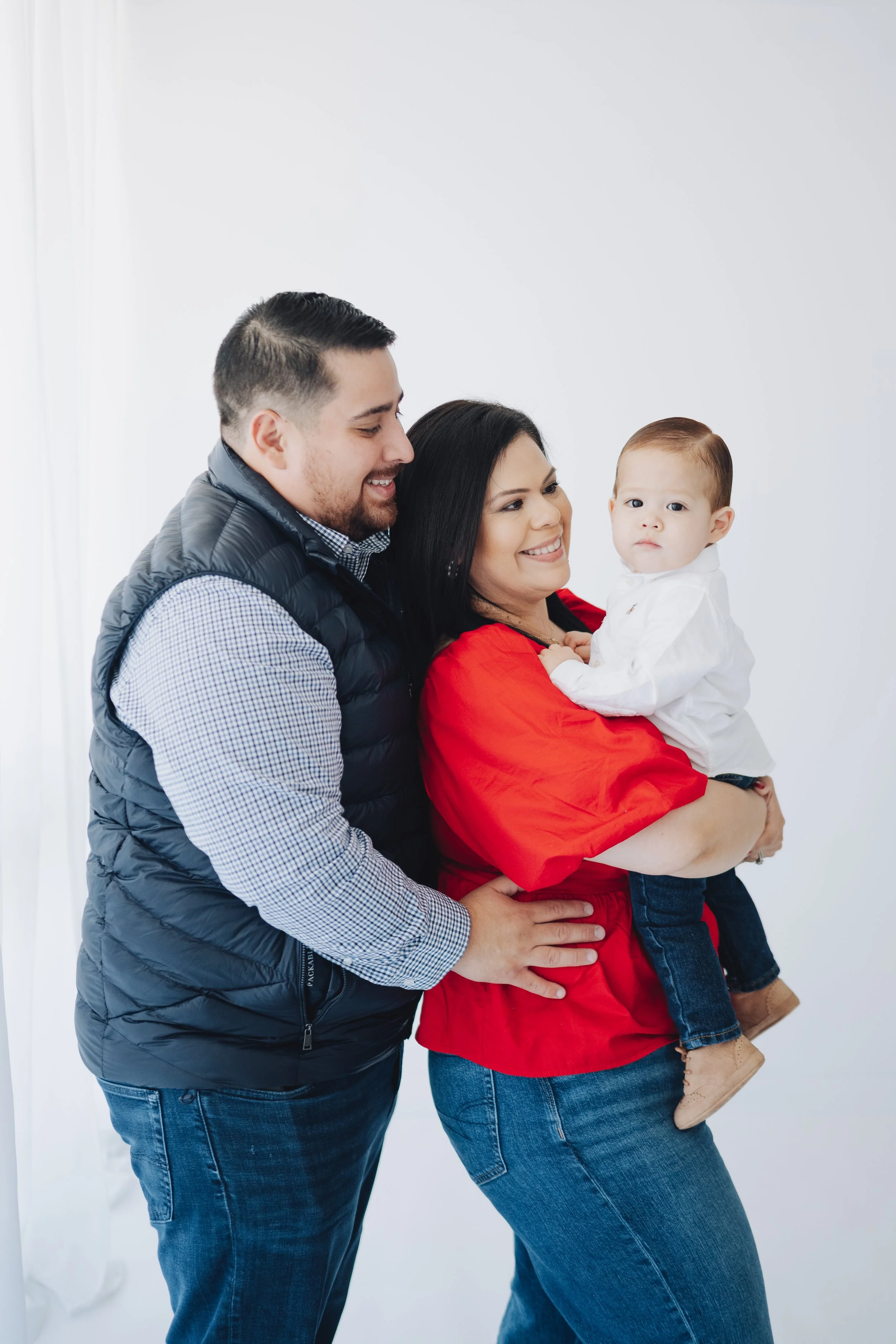 Family of three, woman holding a toddler, on a plain white background, smiling and enjoying time together.