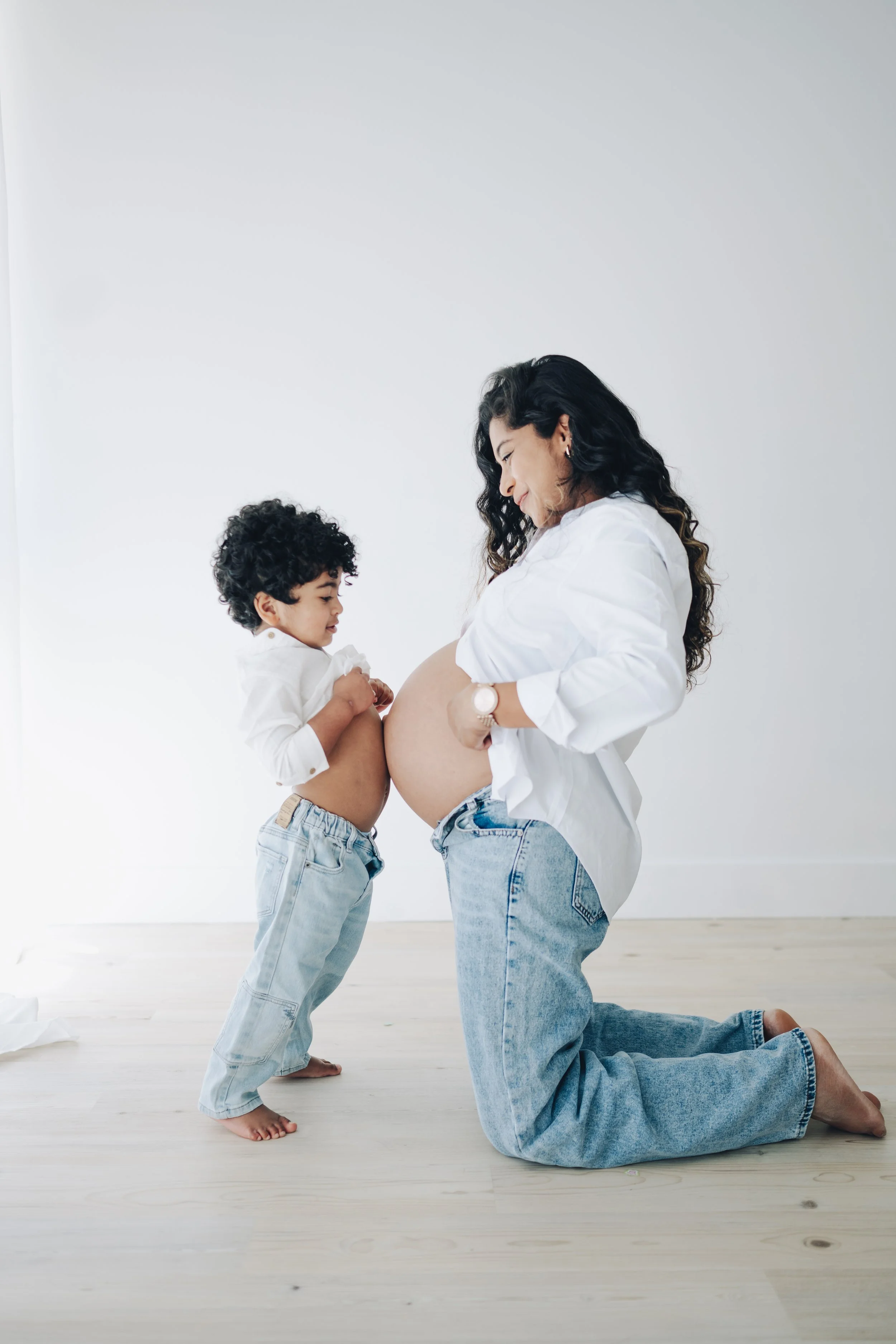 Pregnant woman sitting on a white couch, cradling her belly, with a man beside her gently touching her pregnancy.