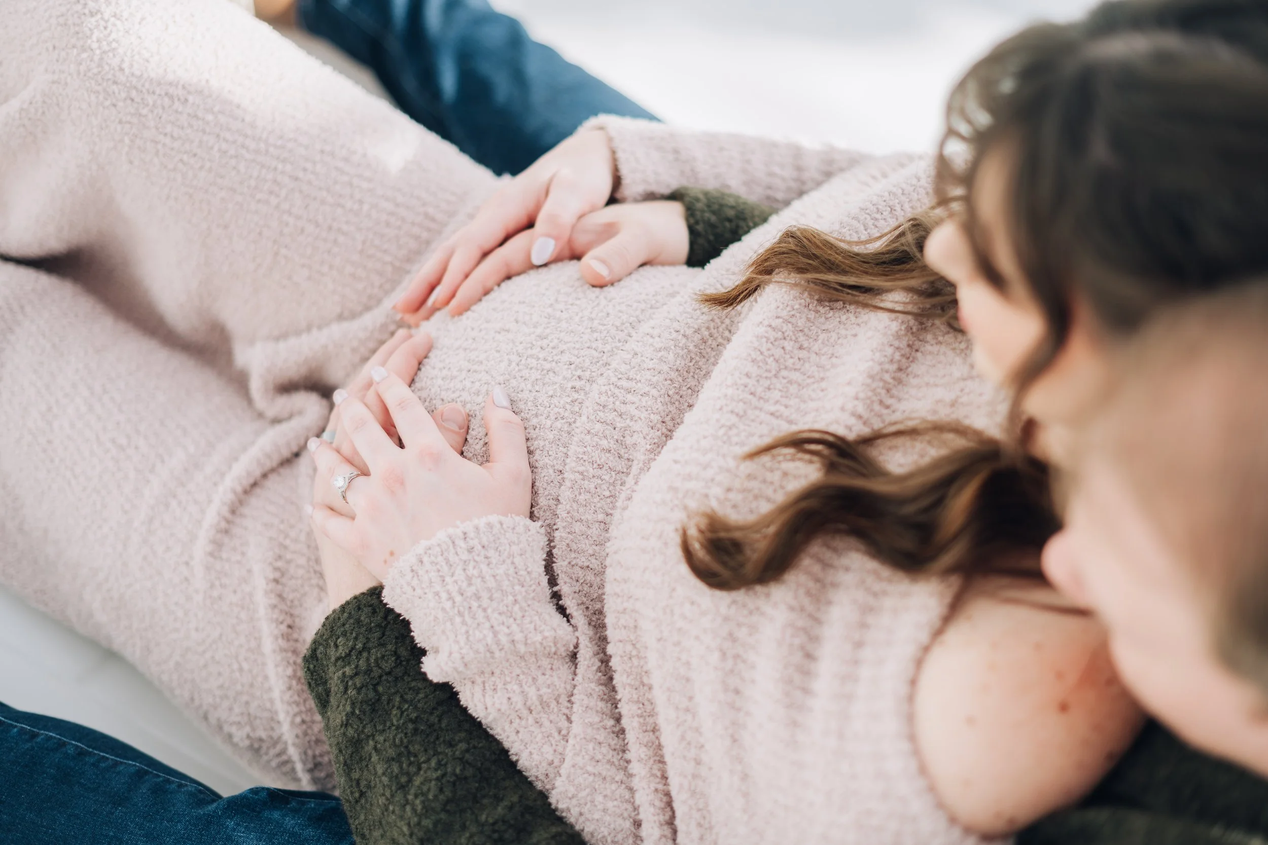 A person lying down on a hospital bed and receiving a prenatal check-up, with a woman placed her hand on the pregnant belly, and a doctor performing an ultrasound scan.