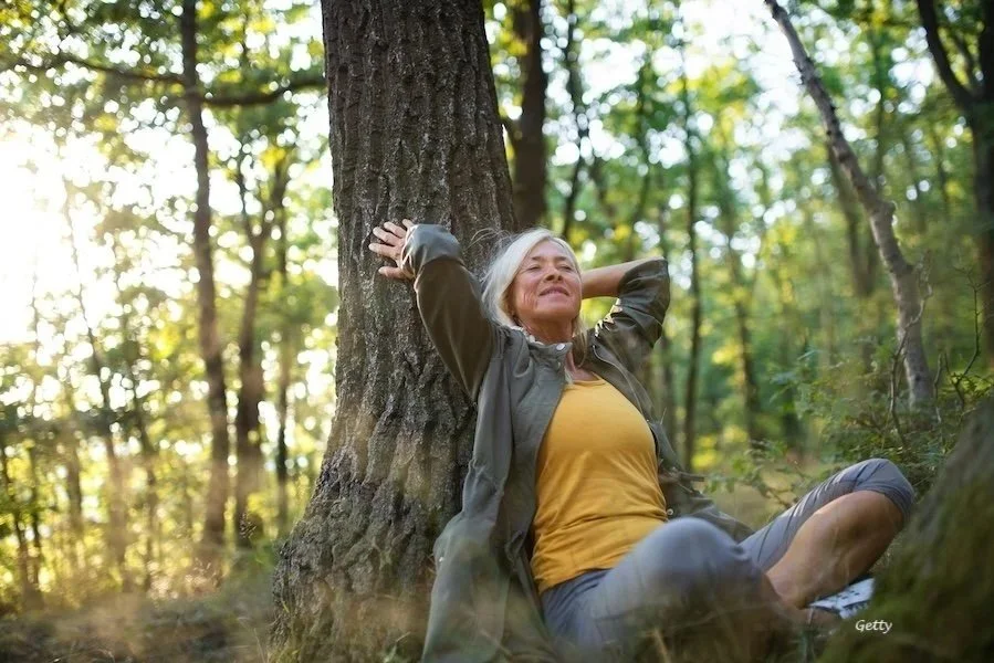 A woman leaning against a tree practicing the art of living alone.