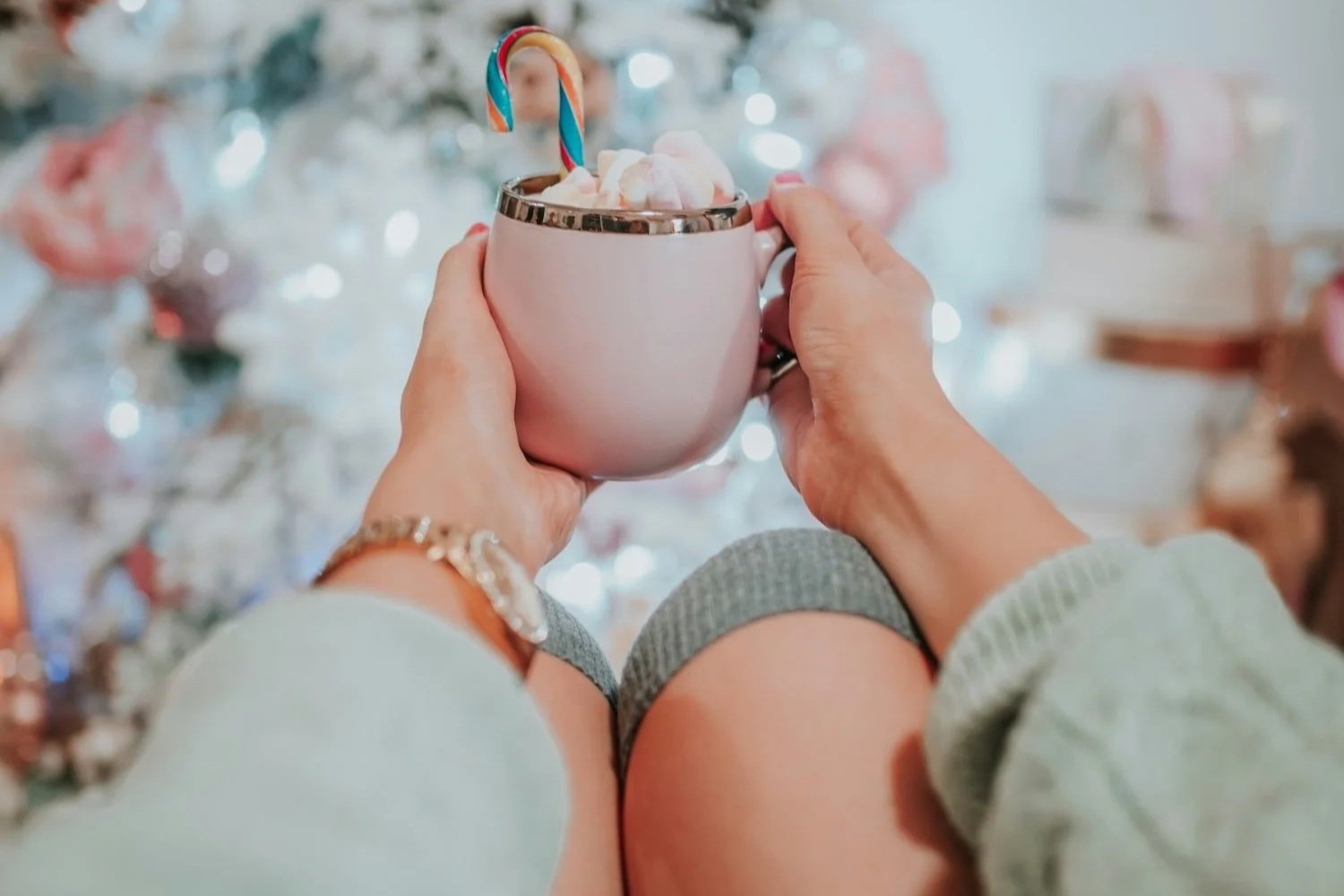 A woman over 55 sitting in front a tree with a hot chocolate showing an example of mindset shifts do they don't stress about Christmas.