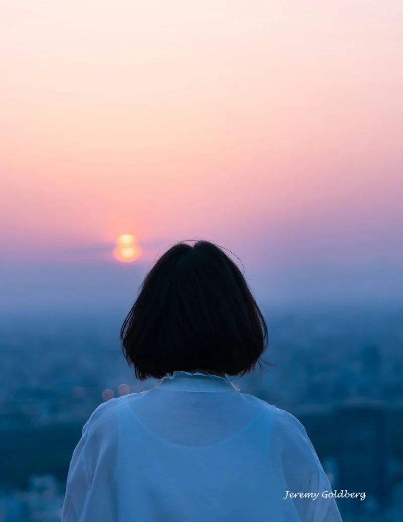 A woman over 55 staring into the sunrise.
