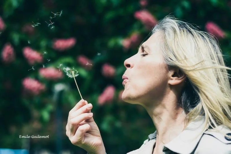 A woman blowing on a dandelion.