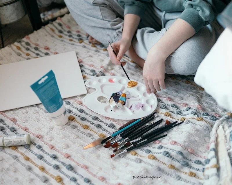 A woman painting on a rug on the floor.