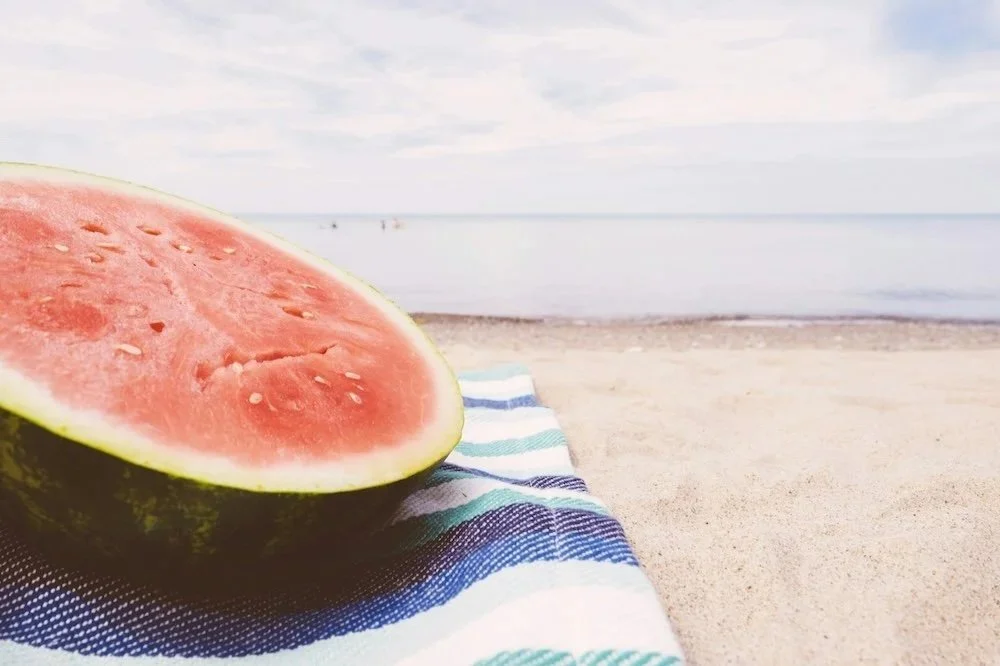 A half a watermelon on a blanket on a beach showing  a way to beat the summer slump.