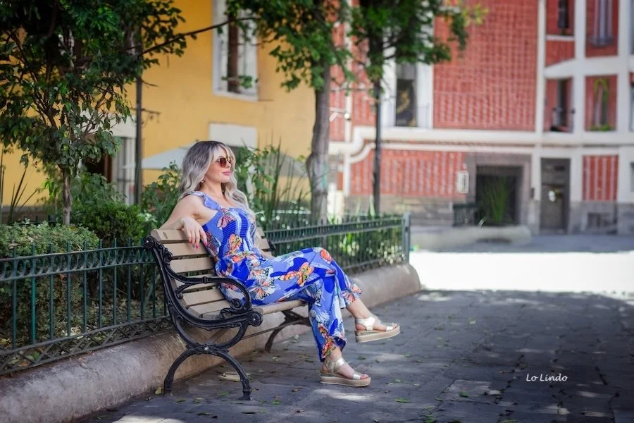 A woman over 55 sitting on a bench in the shade as she practices summer health and wellness.