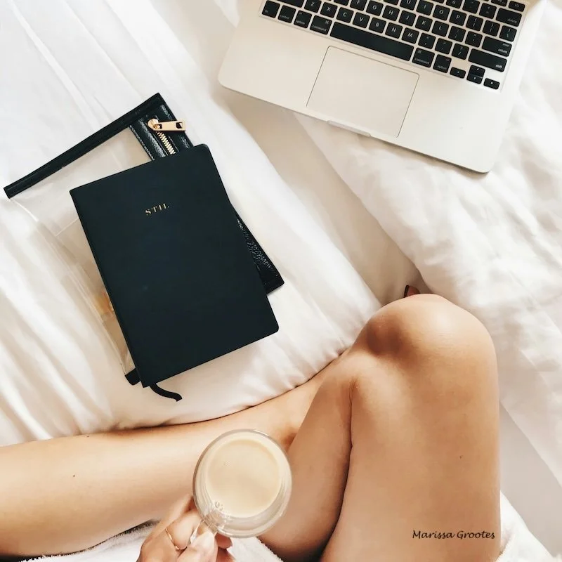 A woman on her bed with a coffee, agenda and computer.