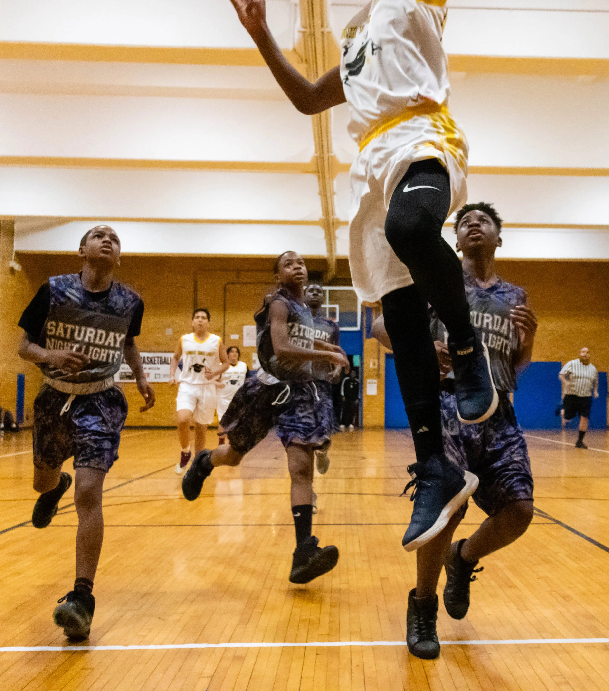 Young female basketball player jumping for a shot while other players watch during a game in a gymnasium.