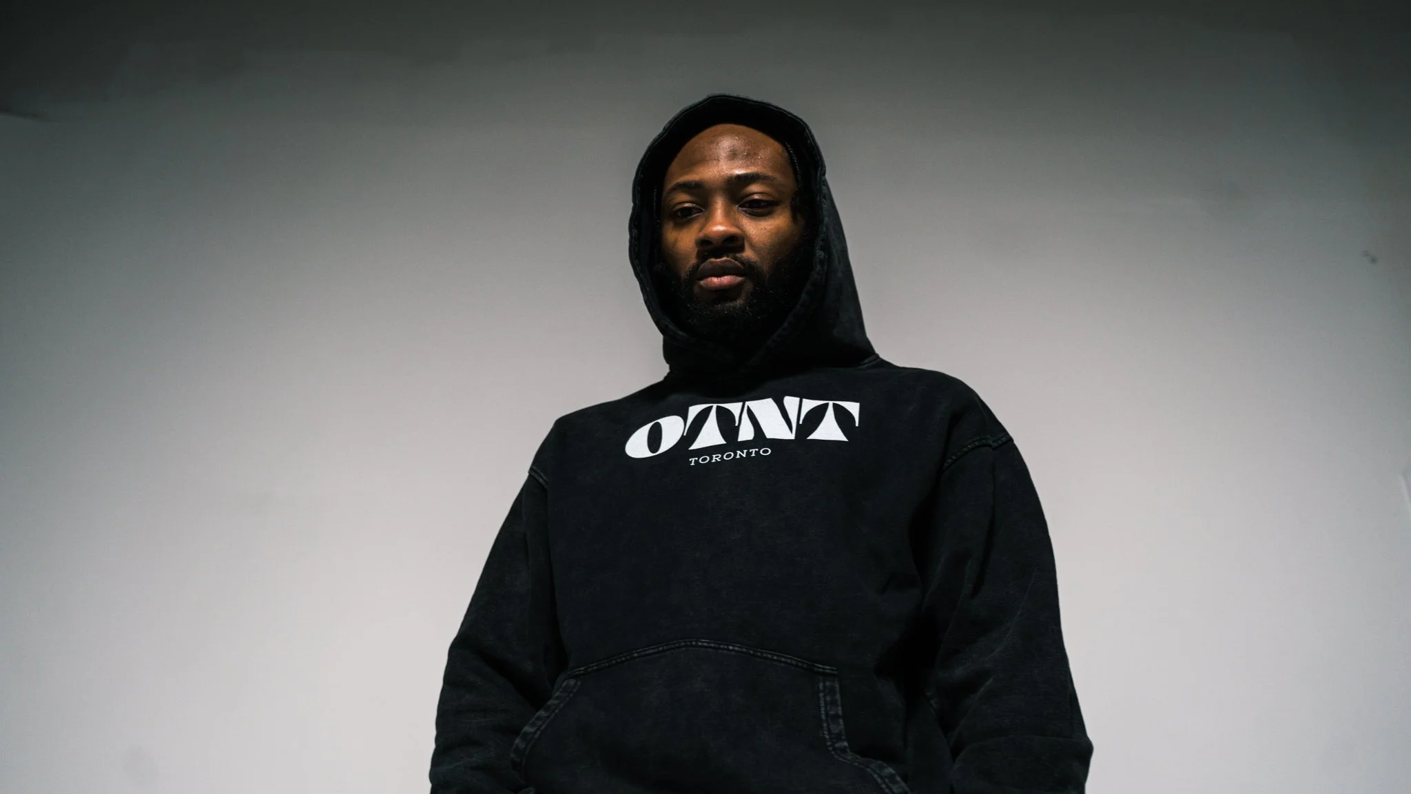A man wearing a black hoodie with the words 'OTN'T Toronto' printed on it, standing indoors against a plain, light-colored wall.