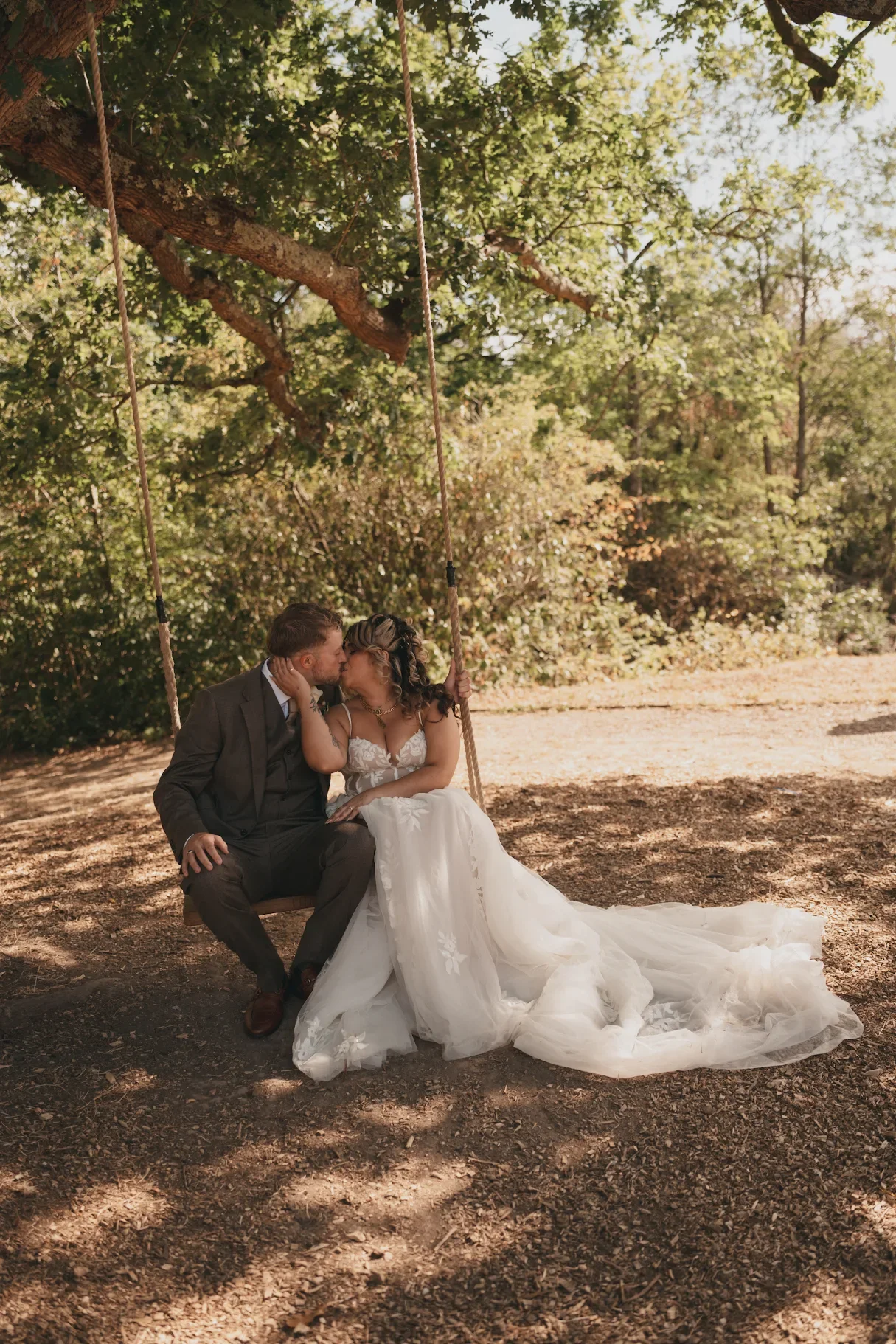 A bride and groom smiling at each other indoors during their wedding, with the bride holding a bouquet of white roses and greenery.
