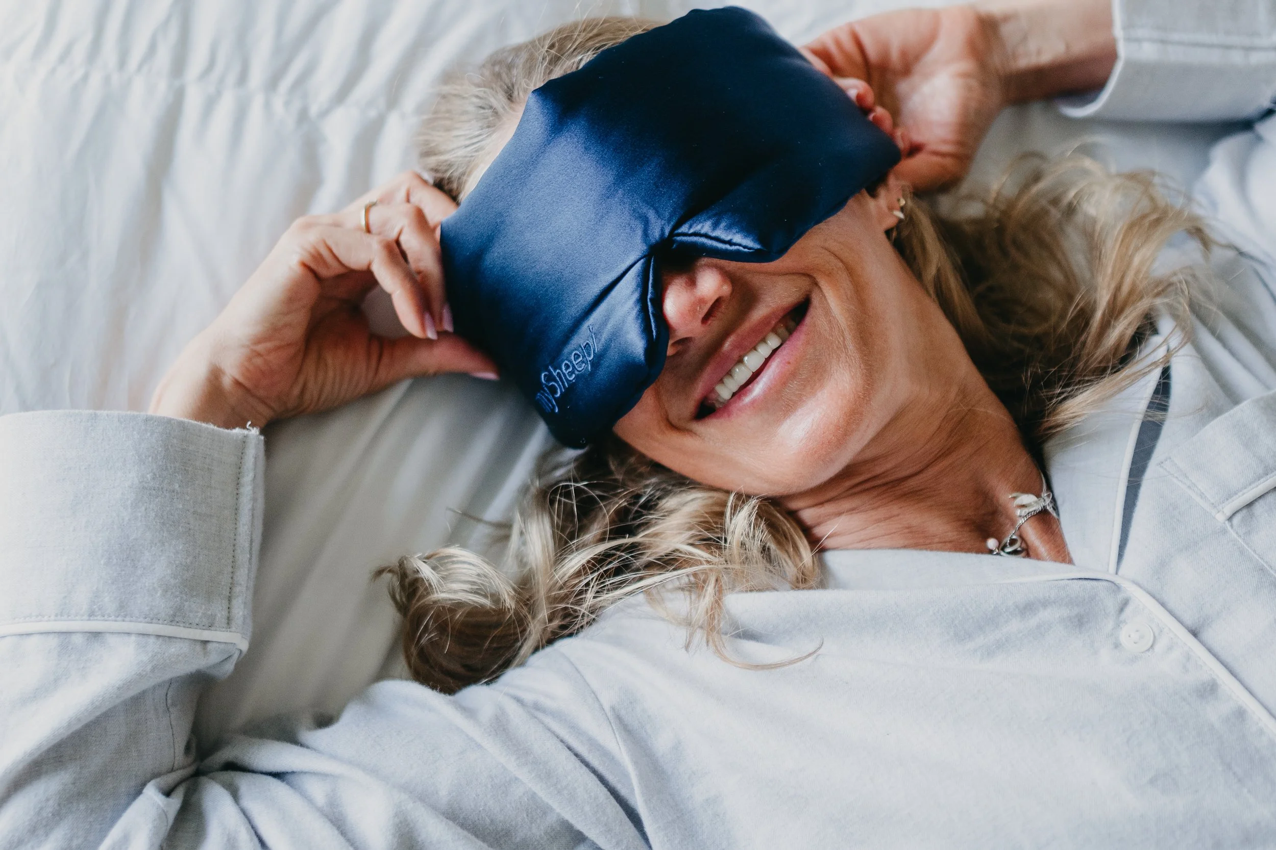 Personal branding photography of a woman smiling while wearing an eye mask, representing wellness and slow living.