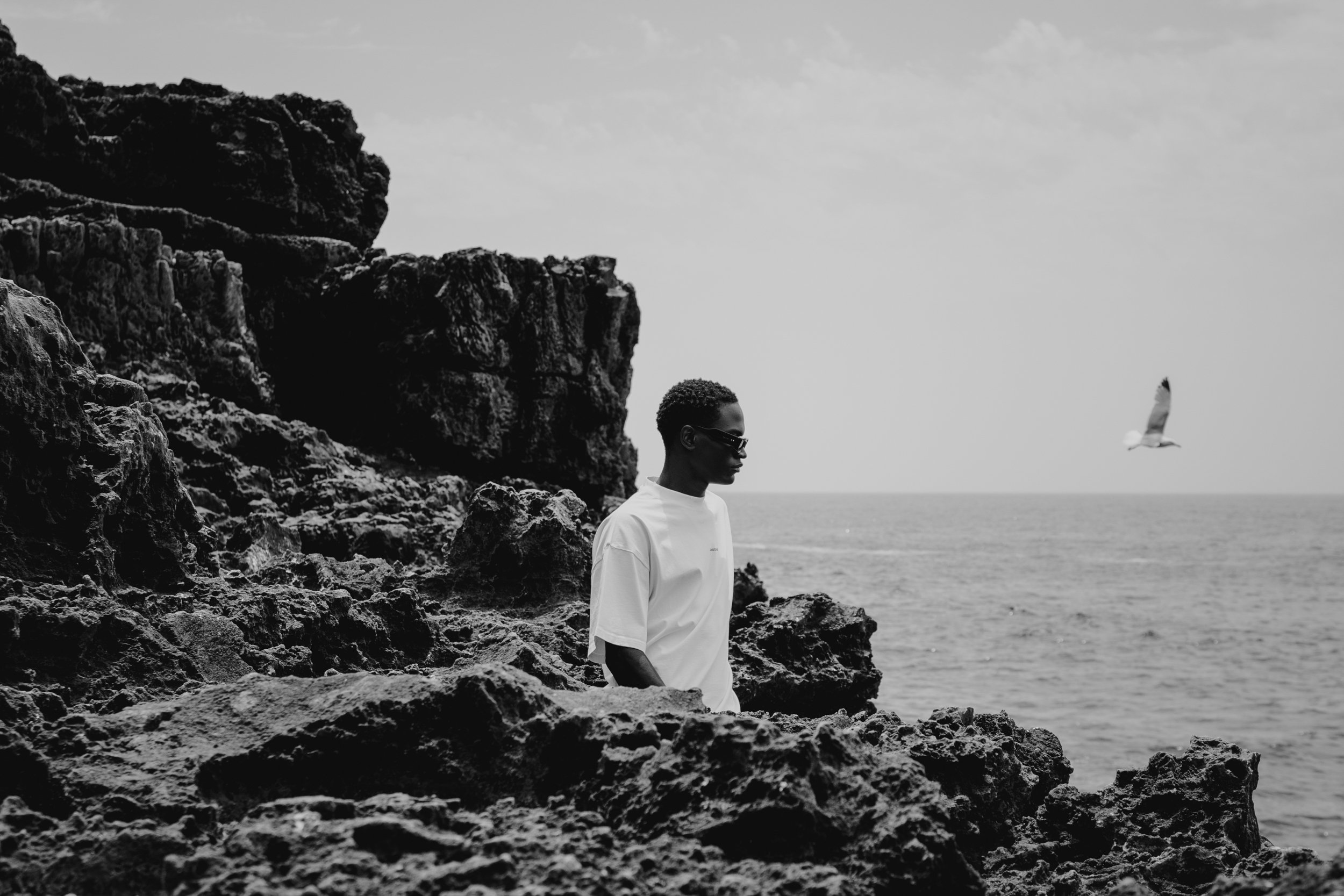Black and white editorial brand photography of a man standing on coastal rocks, creating a minimalist and timeless mood.
