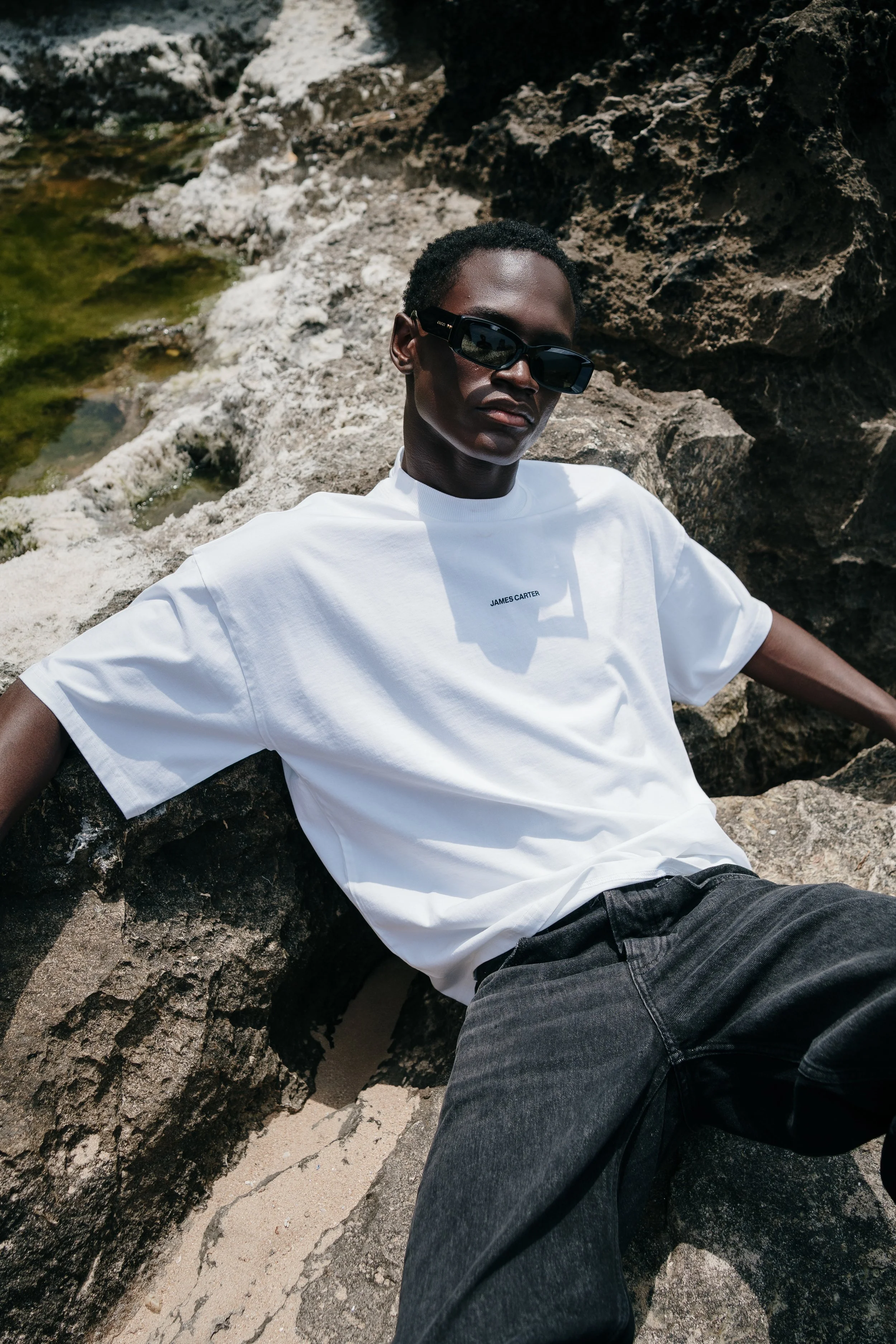 Fashion branding photography of a man dressed in white, photographed outdoors on rocky terrain in Lisbon.
